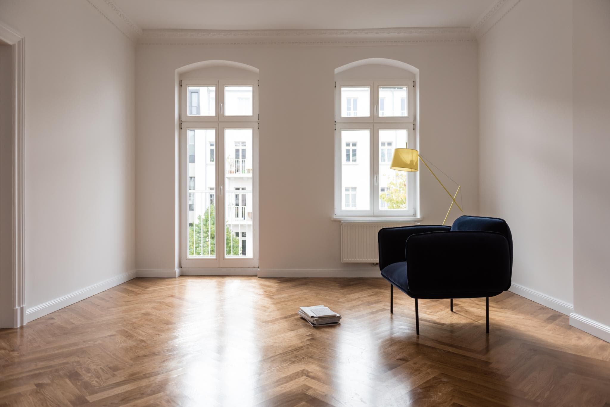 The image features a spacious, empty room with a hardwood floor. In the center of the room, there is a black chair, which appears to be a modern chair. The chair is positioned in front of a window, allowing natural light to enter the room.
A lamp is placed on a stand near the chair, adding a touch of warmth and ambiance to the space. The room also has a window, which provides a view of the outside. The overall atmosphere of the room is clean and minimalistic, with the focus on the black chair and the lamp.