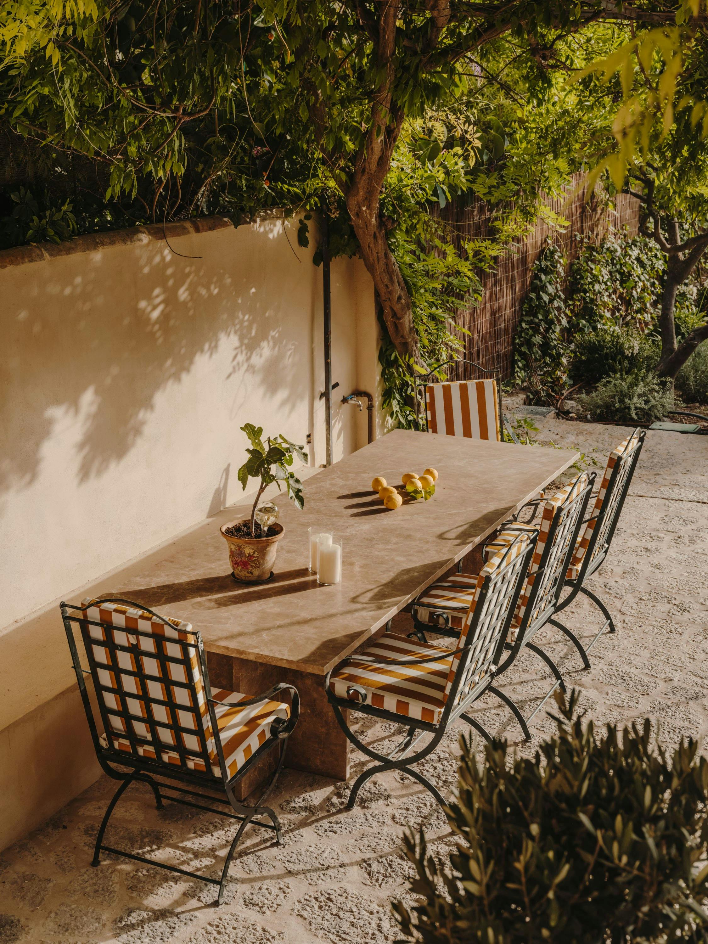 The image features a patio area with a wooden table and chairs set up for a meal. The table is surrounded by chairs, with one chair placed closer to the left side of the table and another chair situated on the right side. A potted plant is placed near the table, adding a touch of greenery to the scene.

In addition to the table and chairs, there are two bowls on the table, one closer to the left side and the other closer to the right side. A vase is also present on the table, enhancing the overall aesthetic of the patio