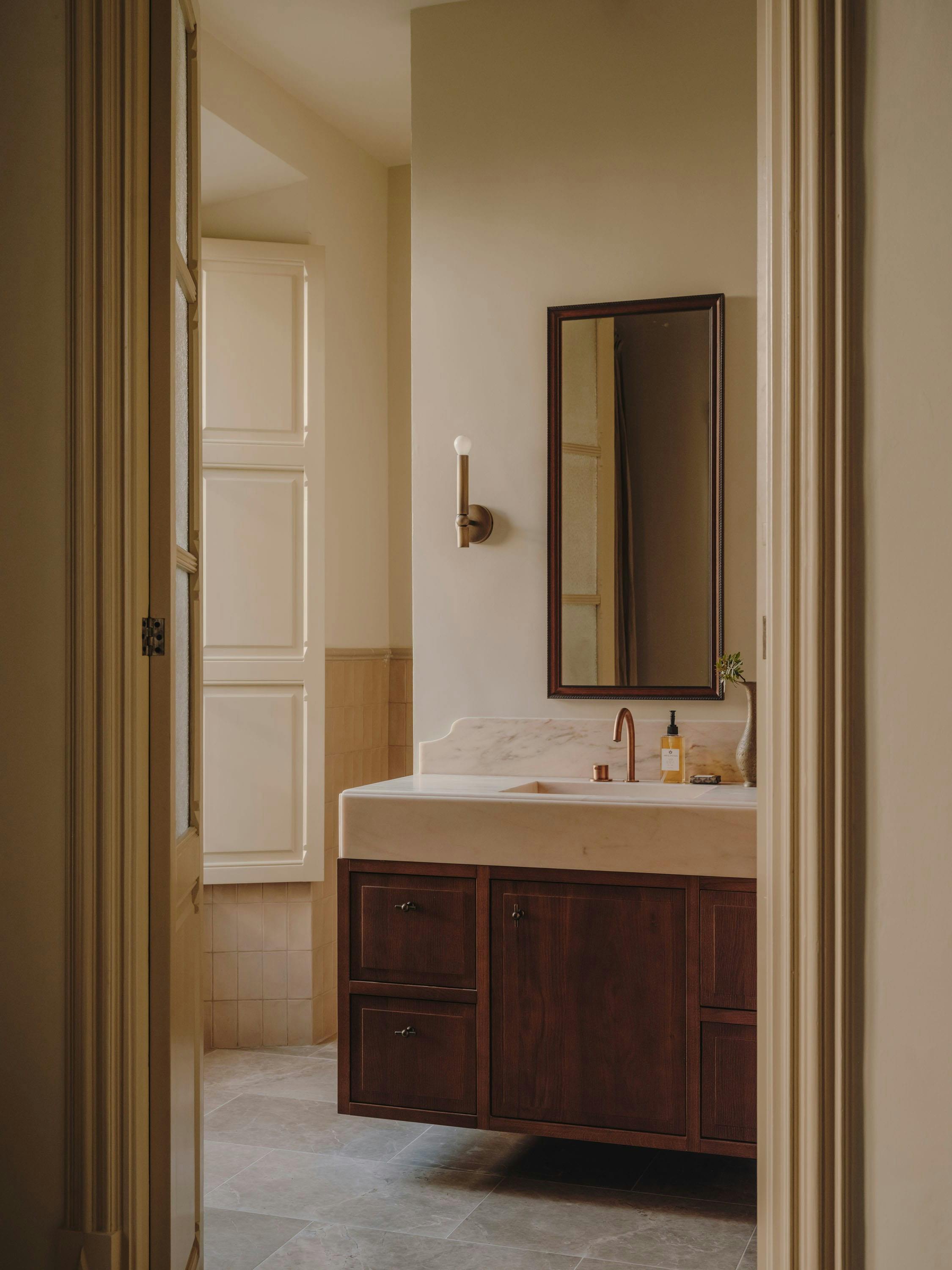 The image features a bathroom with a large sink and a mirror above it. The sink is situated in the center of the room, and the mirror is placed above it. The bathroom appears to be clean and well-maintained.

In addition to the sink and mirror, there are two bottles placed on the countertop, likely containing toiletries or personal care products. A potted plant is also present in the bathroom, adding a touch of greenery to the space. The bathroom is open to the hallway, which can be seen in the background.