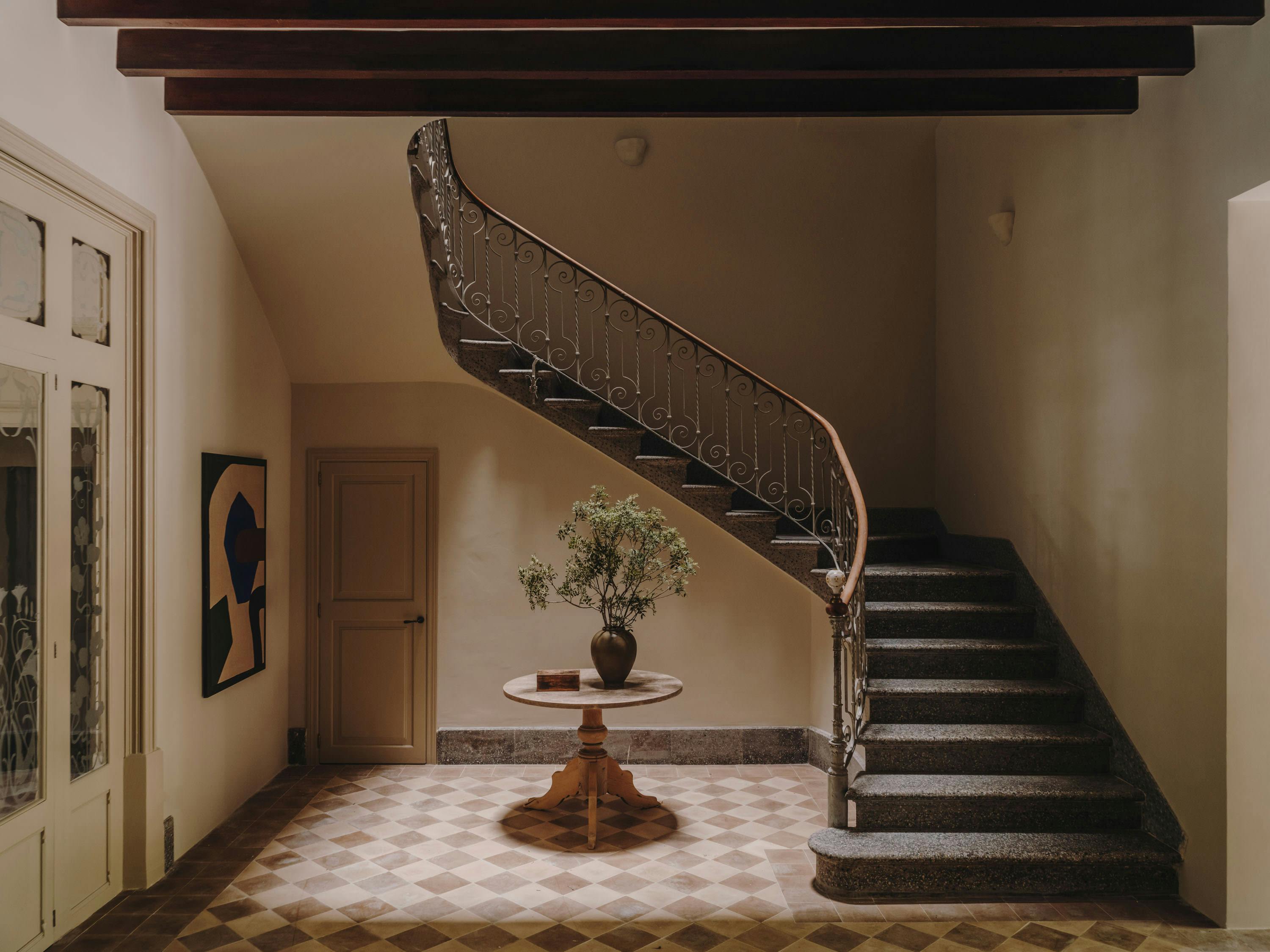 The image features a hallway with a staircase leading to a doorway. The staircase is made of metal and has a spiral design. The hallway is decorated with a potted plant placed on the floor near the bottom of the stairs. 

In the hallway, there is a vase on a table, which adds a touch of elegance to the space. Additionally, there are two pictures hanging on the wall, one on the left side and another on the right side of the hallway. The presence of these pictures and the potted plant create a cozy and inviting