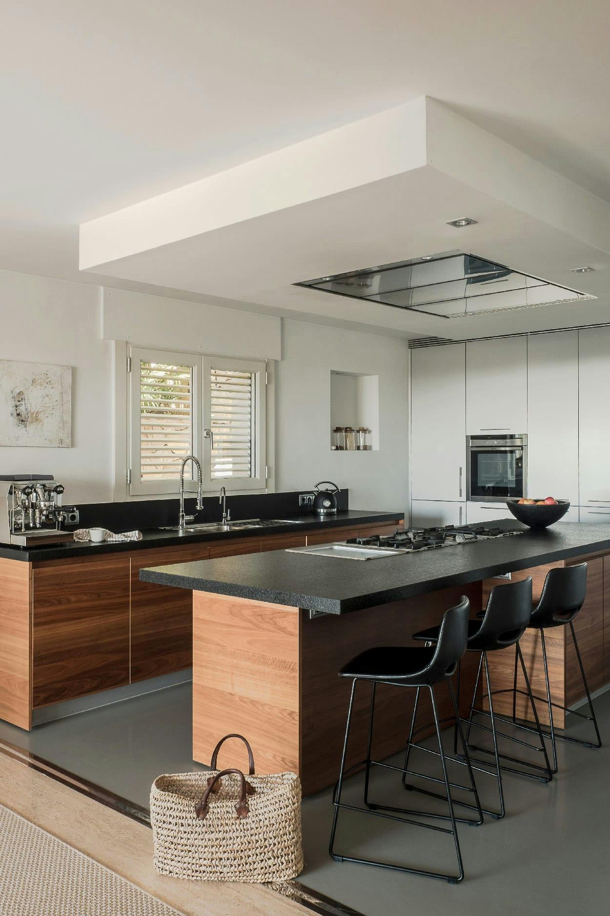 The image showcases a modern, spacious kitchen with a black countertop and a black island. The kitchen is equipped with various appliances, including a refrigerator, oven, and microwave. There are two sinks, one on the left side of the kitchen and another on the right side. A dining table is located in the middle of the kitchen, surrounded by chairs.

In addition to the kitchen appliances, there are two chairs placed near the dining table, and a handbag can be seen on the left side of the room. The kitchen also features