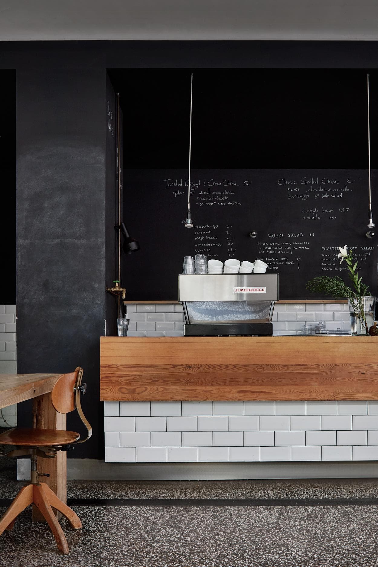 The image features a small, modern kitchen with a black countertop and a white backsplash. The kitchen is equipped with a sink, a refrigerator, and a microwave. There are several cups and bowls placed on the countertop, and a potted plant is also present in the room.