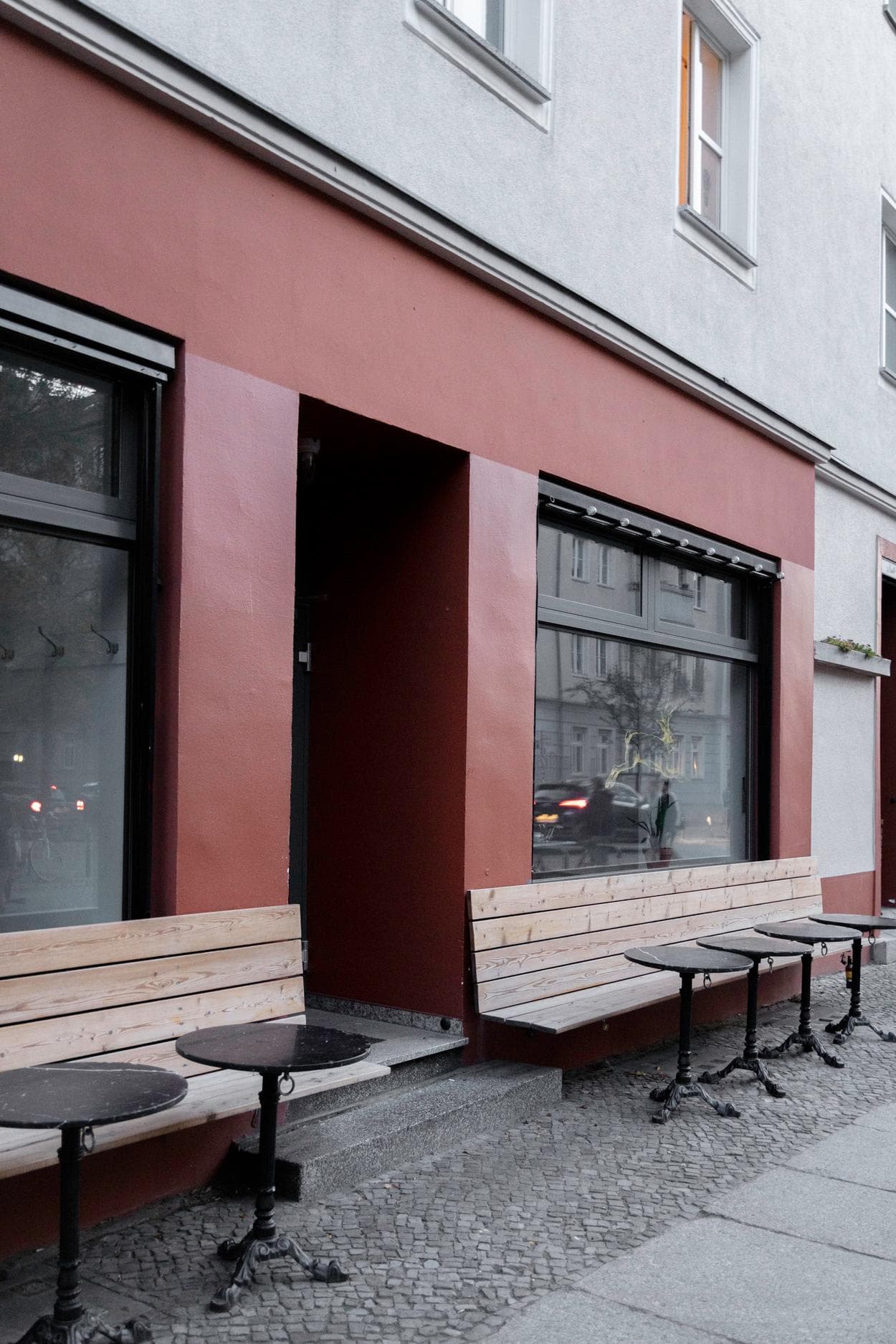 The image features a row of benches outside a building, with a brick walkway and a red door.