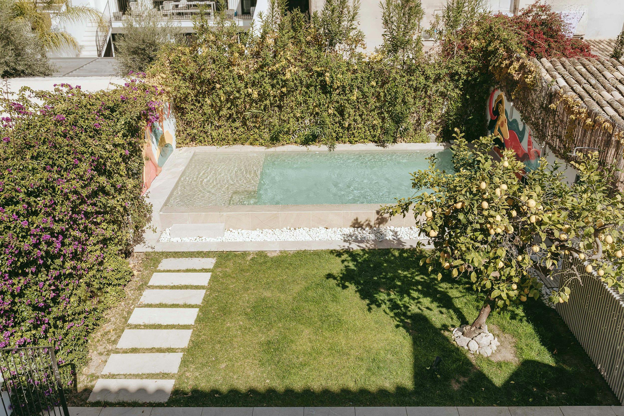 The image features a large, well-maintained backyard with a swimming pool, a patio, a garden, and a house.