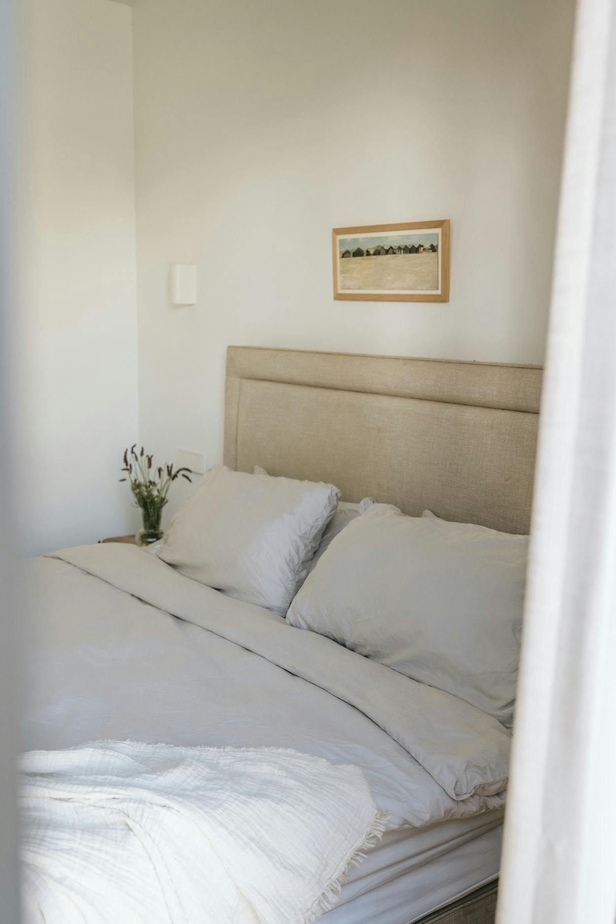 The image features a neatly made bed with a white comforter and pillows, placed in a room with a window.