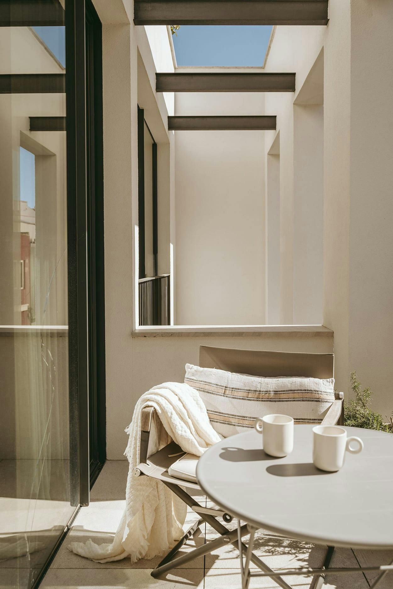 The image features a large, open patio with a white table and chairs, a white table with a cup and a bowl, and a white table with a bowl and a cup. There are two potted plants in the scene, one on the left side and another on the right side of the patio.