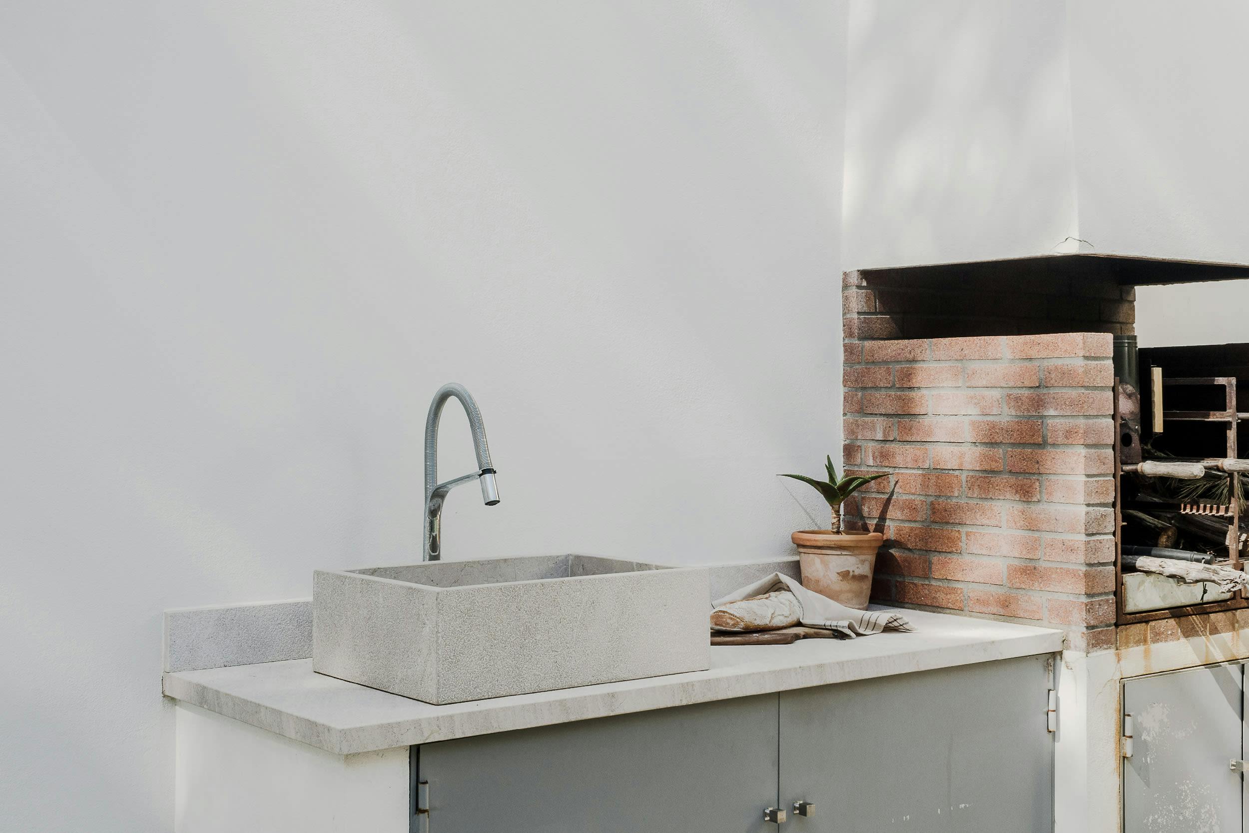 The image features a modern kitchen with a large sink, a stainless steel sink, and a brick oven.