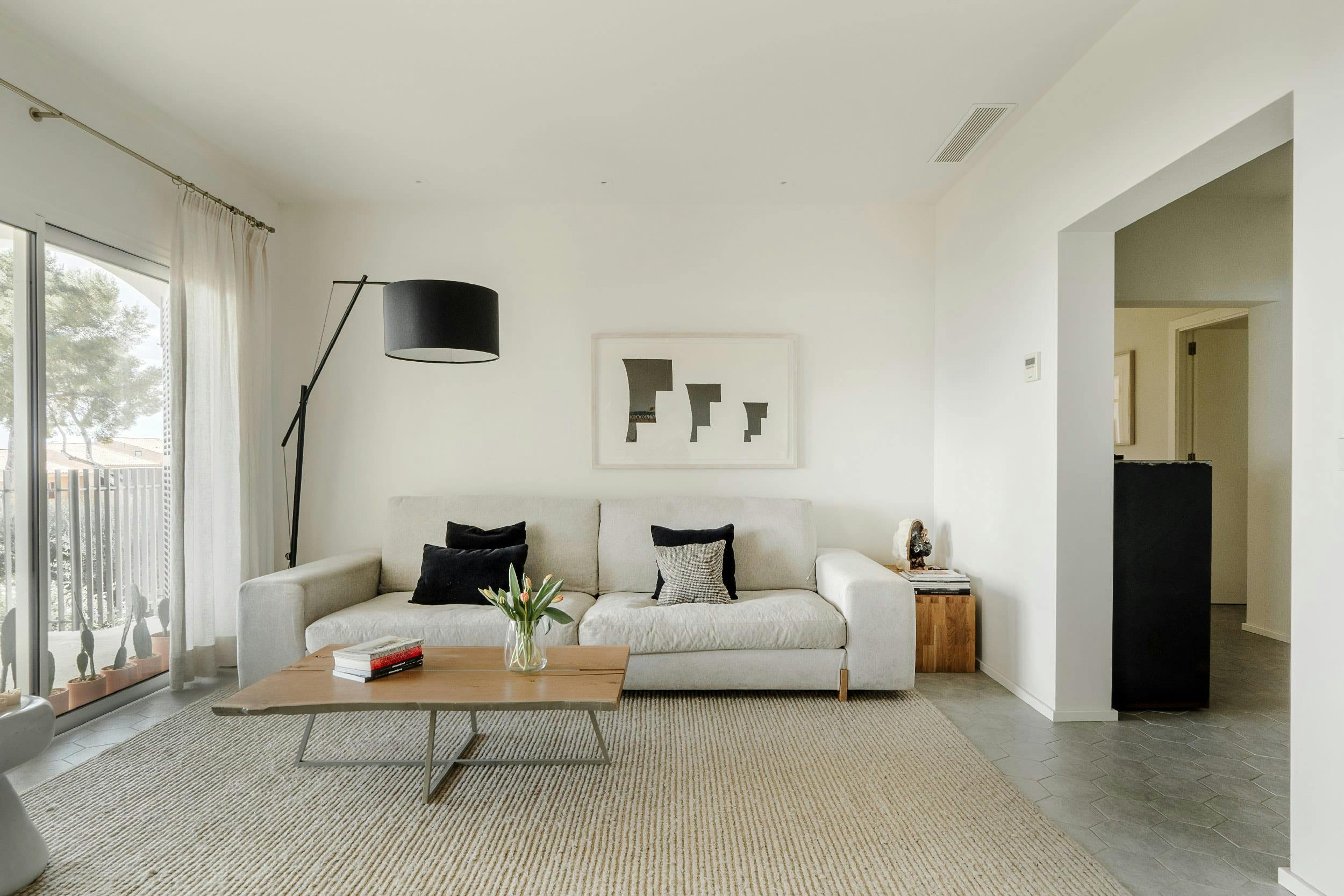 The image features a spacious, modern living room with a white couch, a coffee table, and a television.