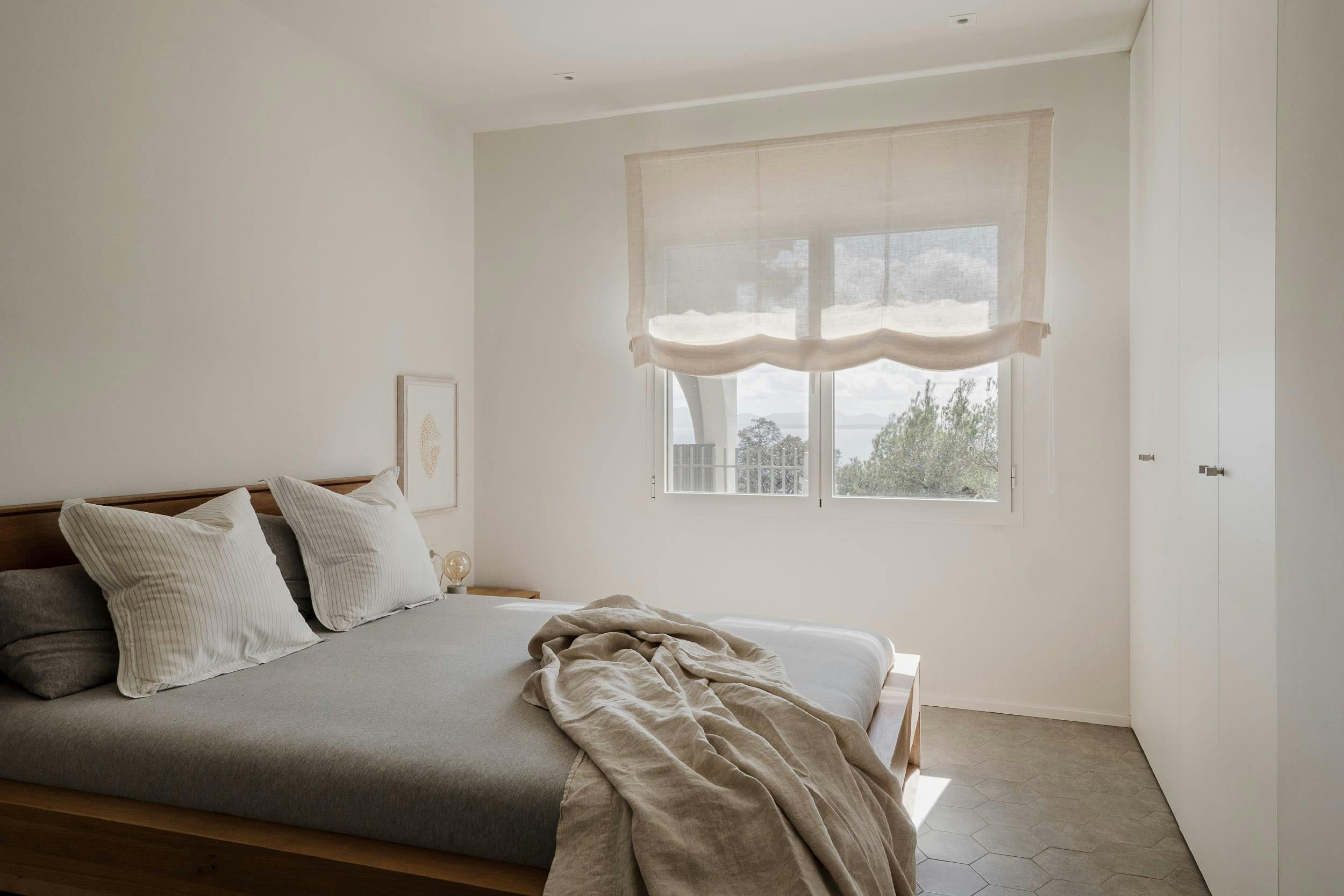 The image features a large bedroom with a neatly made bed, a window, and a white curtain.