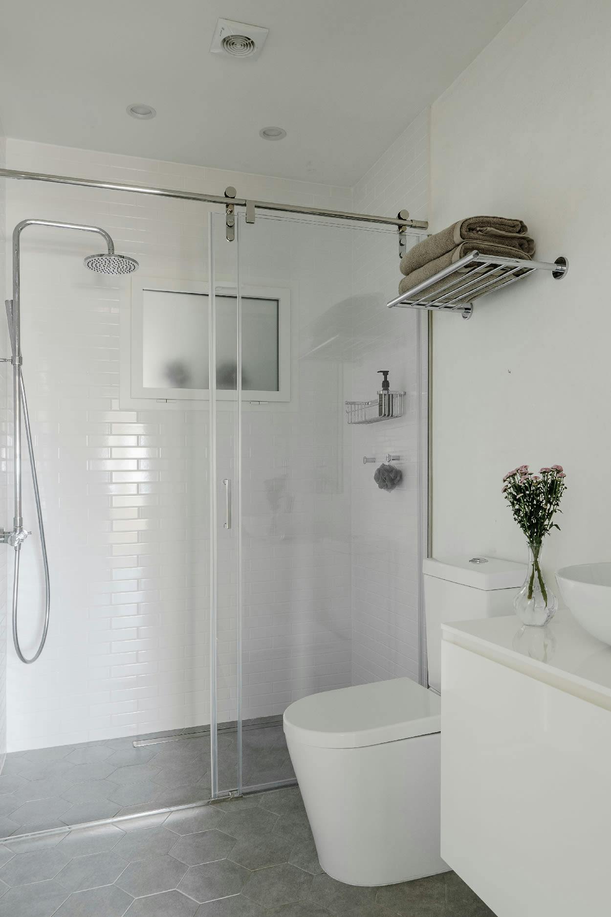 The image features a clean, white bathroom with a white bathtub, toilet, and shower. There is a vase with flowers placed on the counter next to the bathtub, and a sink is also present in the bathroom.