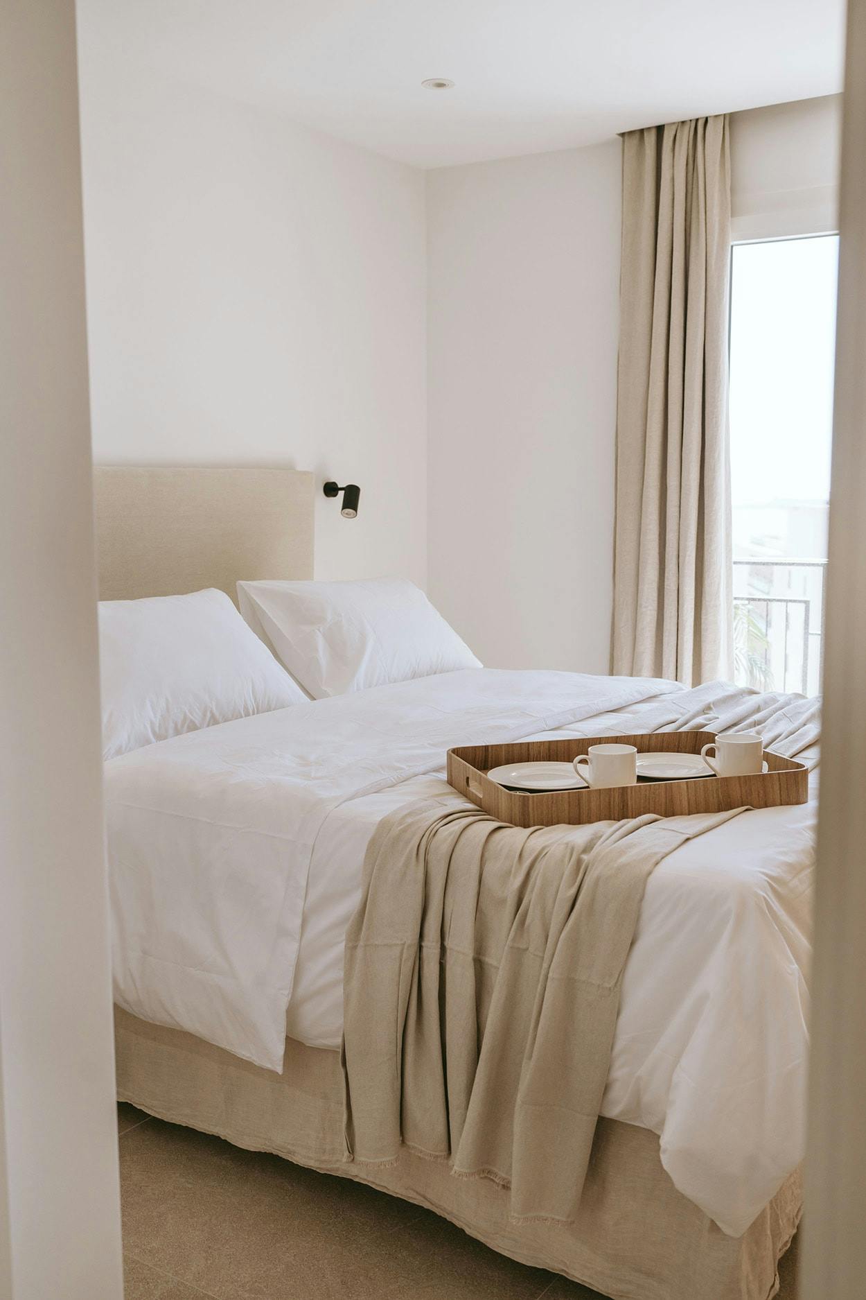 The image features a large, well-made bed with a white comforter and a white headboard, placed in a room with a window.