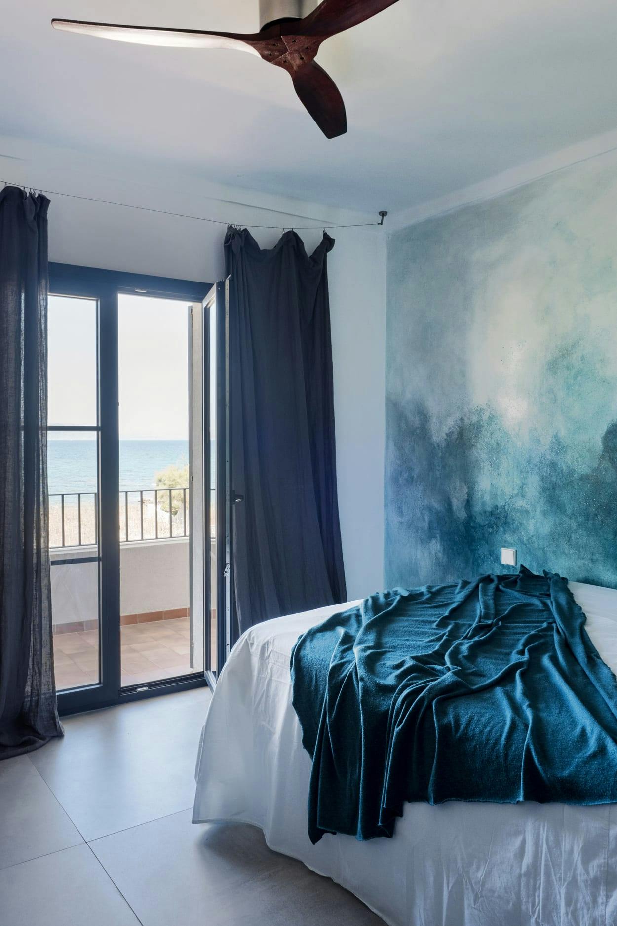 The image features a large bedroom with a neatly made bed, a large painting on the wall, and a ceiling fan.