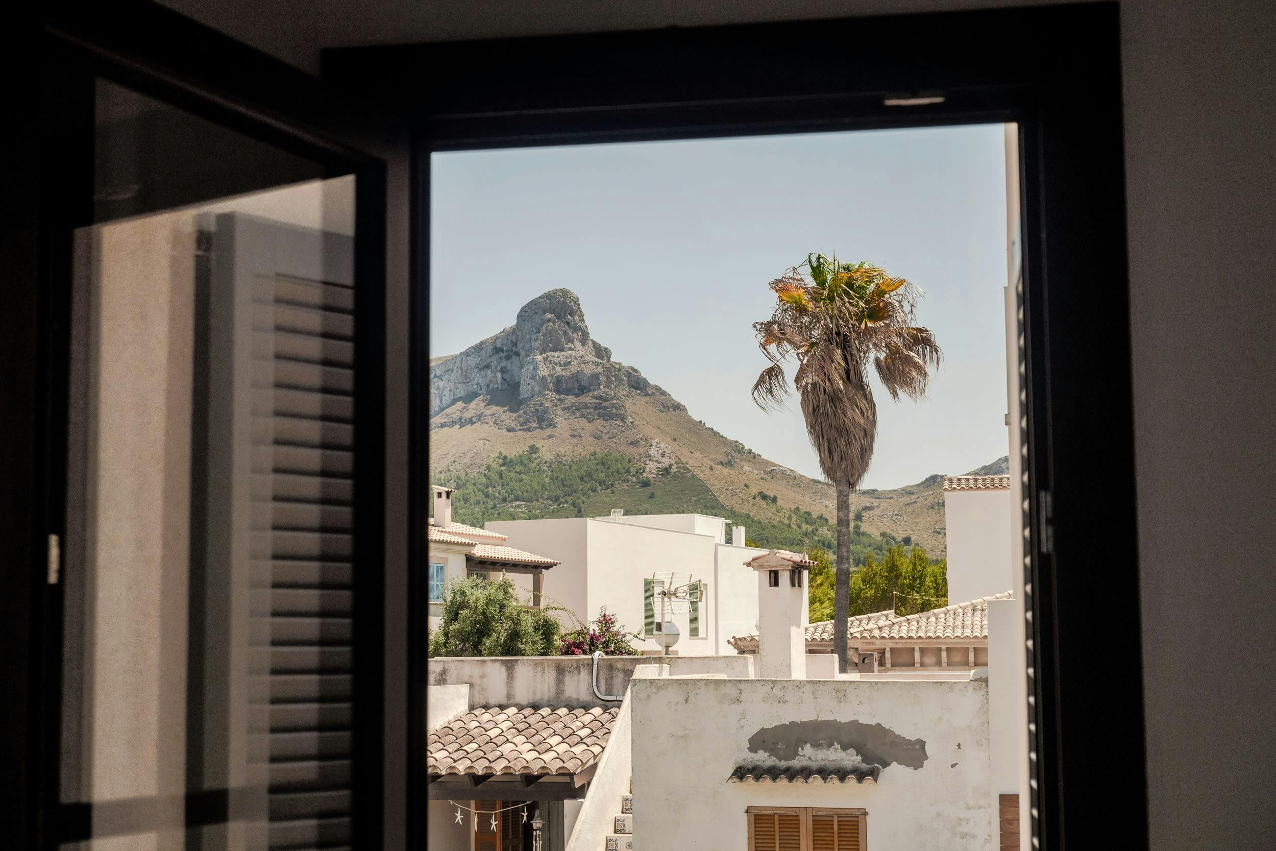 A large window in a building offers a view of a mountain range, with a palm tree in the foreground.
