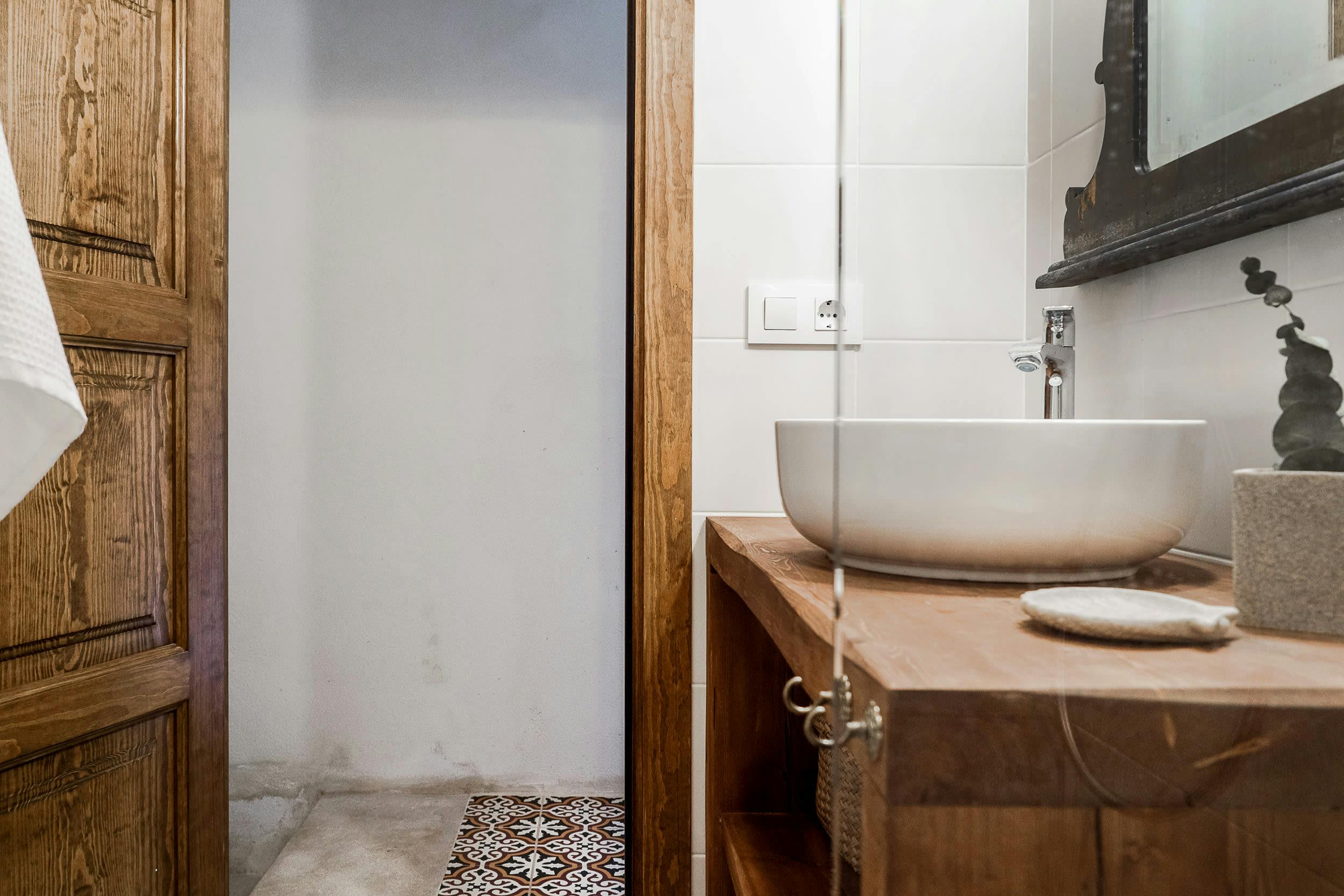 The image features a small bathroom with a white sink, a mirror, and a wooden door.
