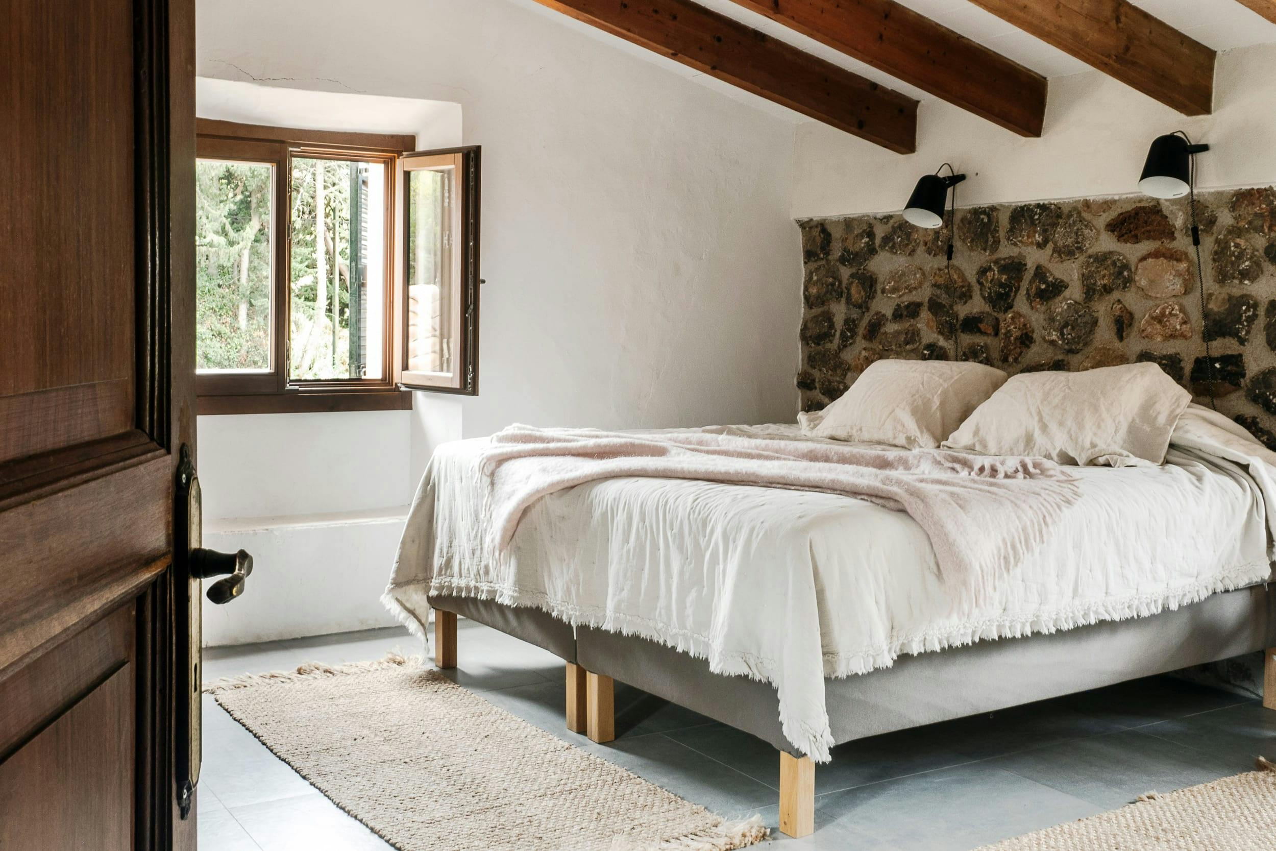 The image features a large bedroom with a neatly made bed, a wooden headboard, and a window.