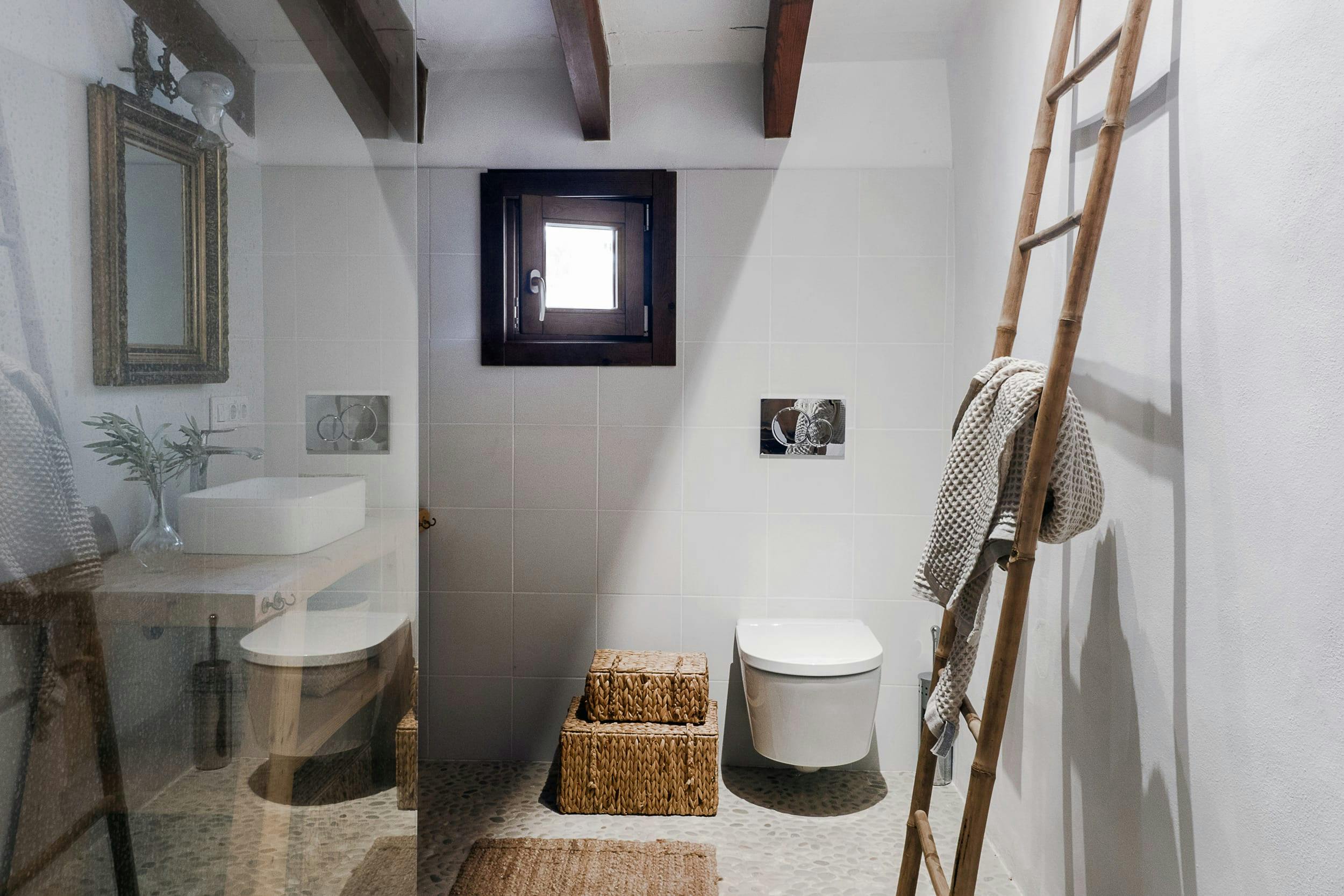 The image features a small bathroom with a white toilet, sink, and window.