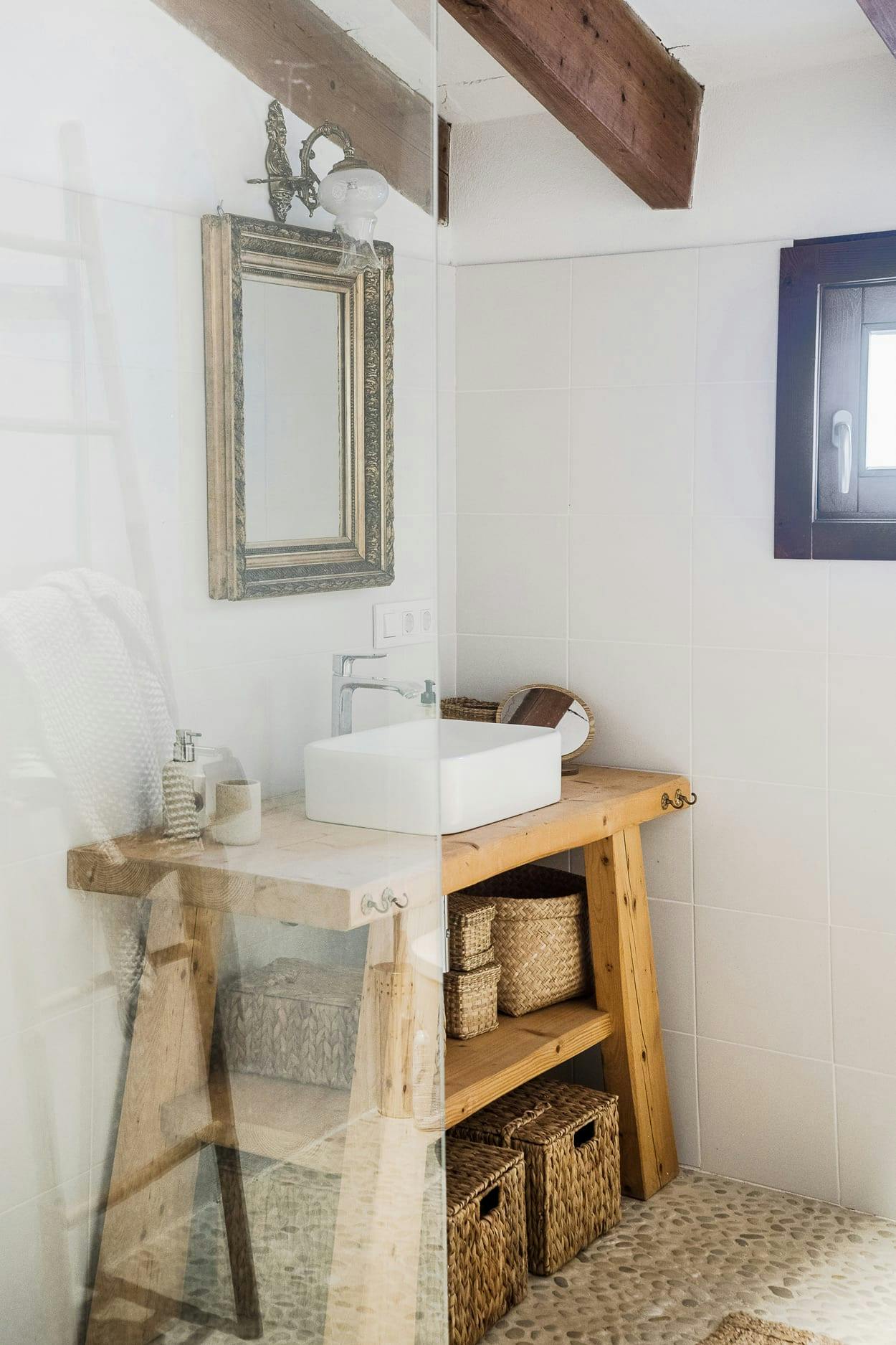 The image features a small bathroom with a white sink, a mirror, a wooden vanity, and a wooden stool.