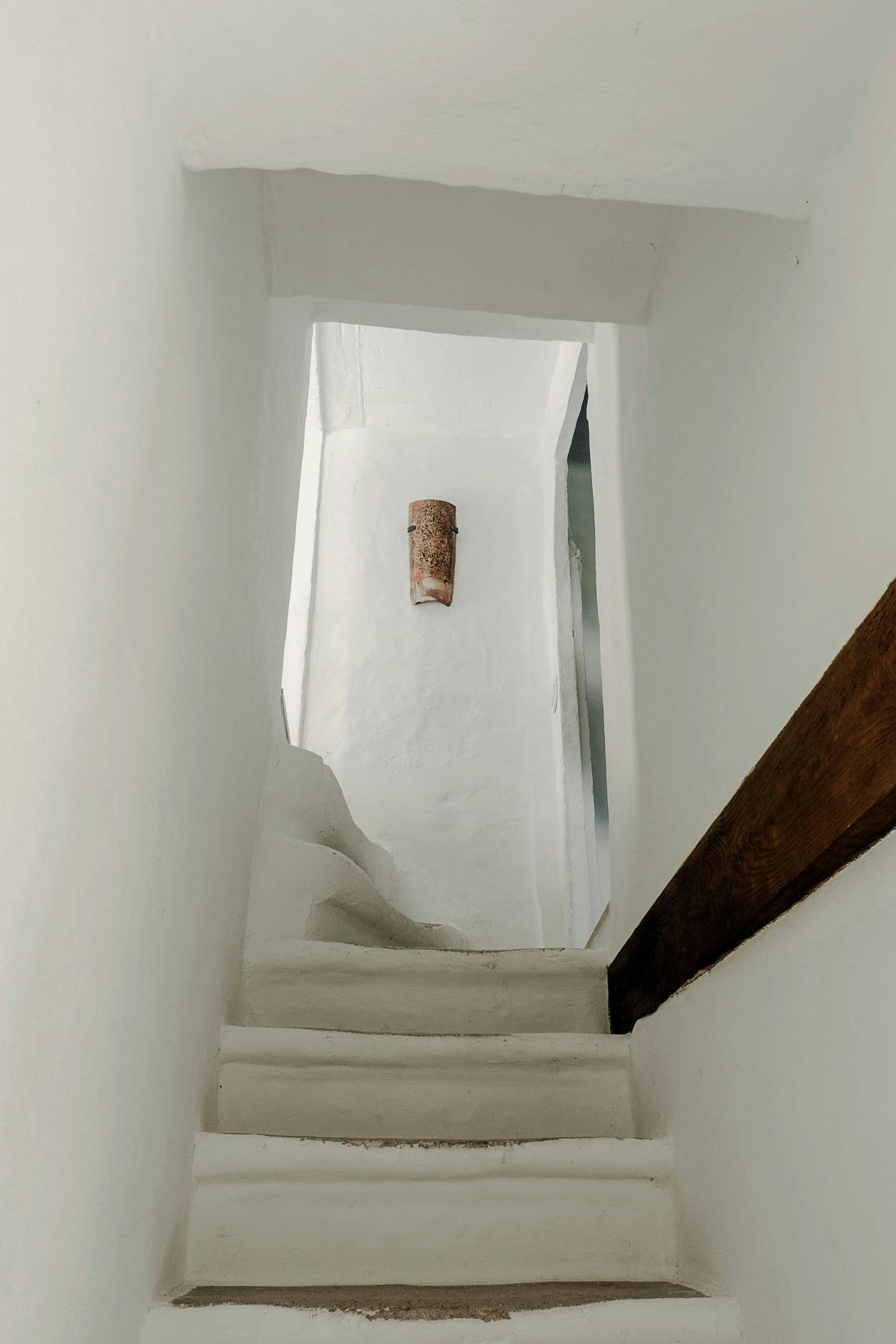 A white staircase with a wooden railing is shown in a white room, with a small window above it.