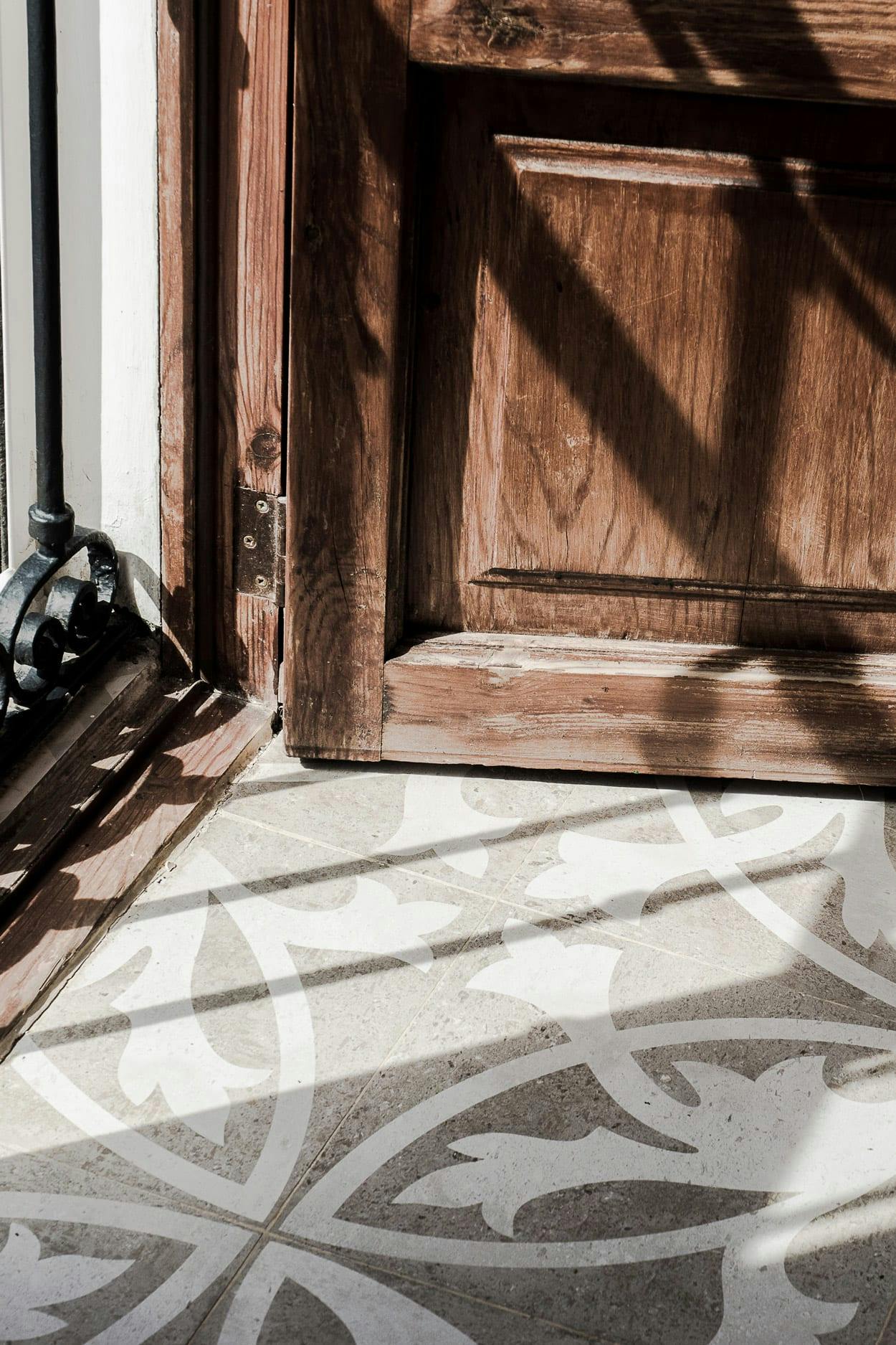 A wooden door with a black and white checkered pattern is open, revealing a shadow on the doorstep.