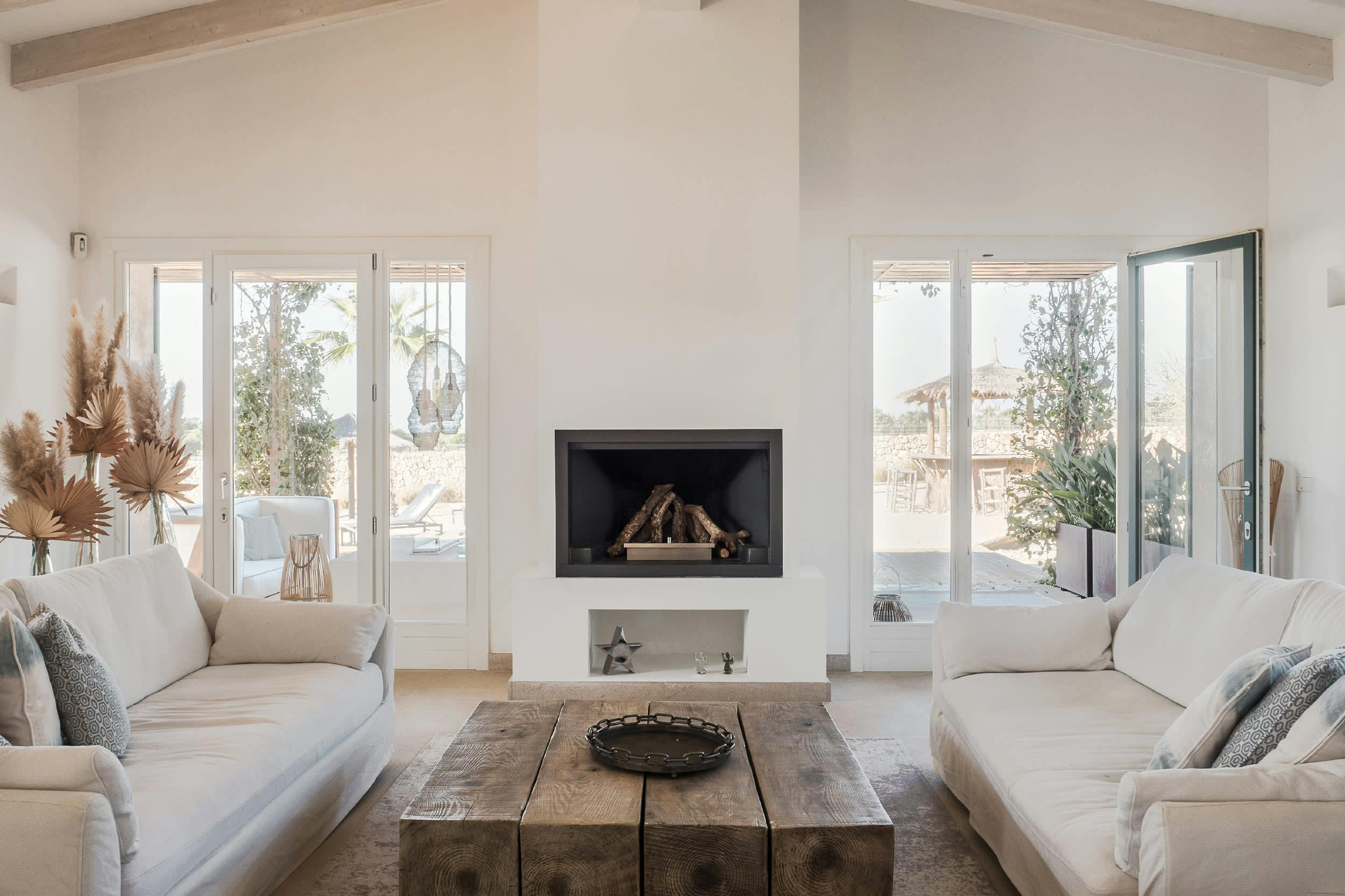 The image features a modern, white living room with a fireplace, a large window, and a couch.