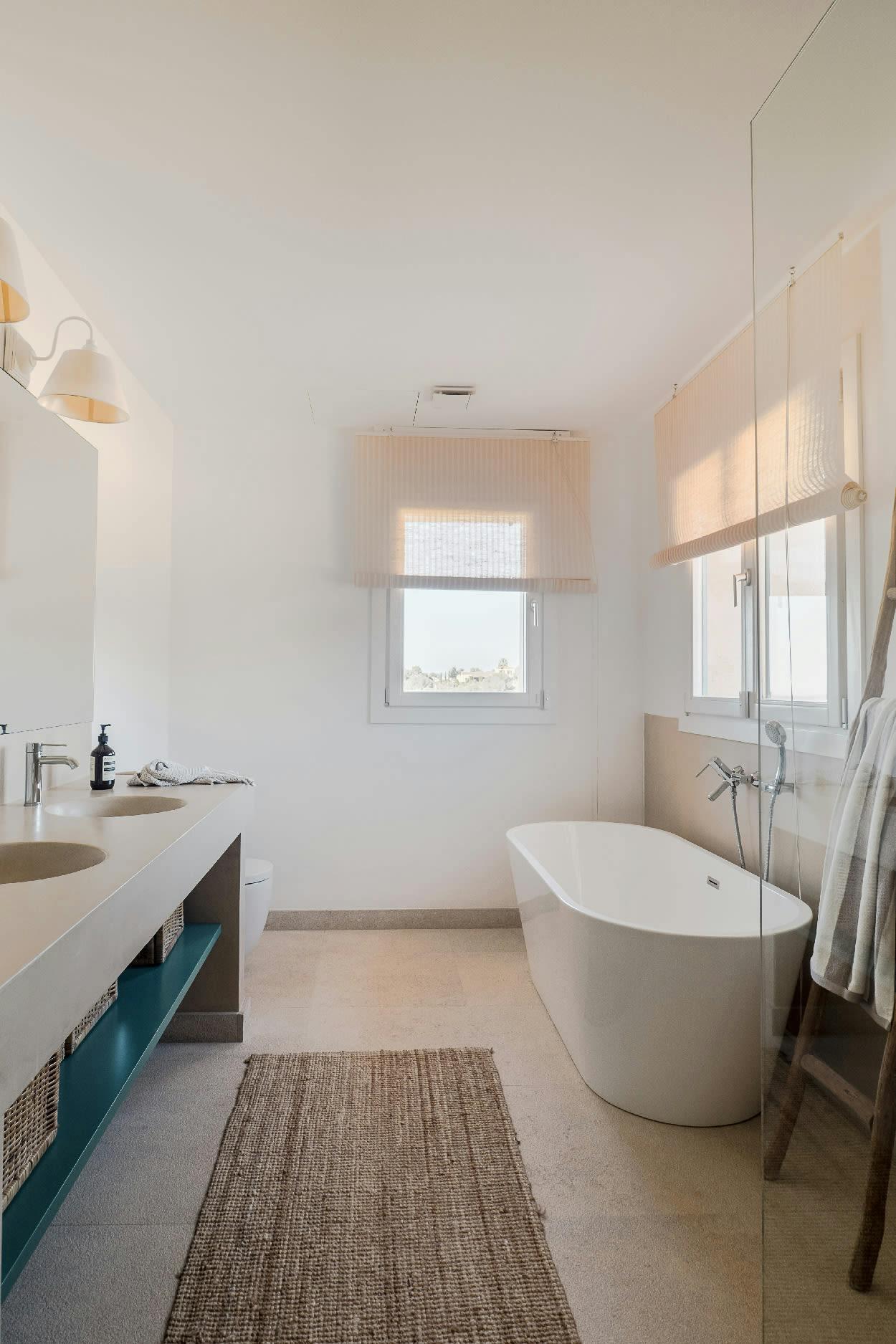 The image features a large, modern bathroom with a white bathtub, sink, and toilet. The bathroom is clean and well-lit, with a rug on the floor and a window nearby.