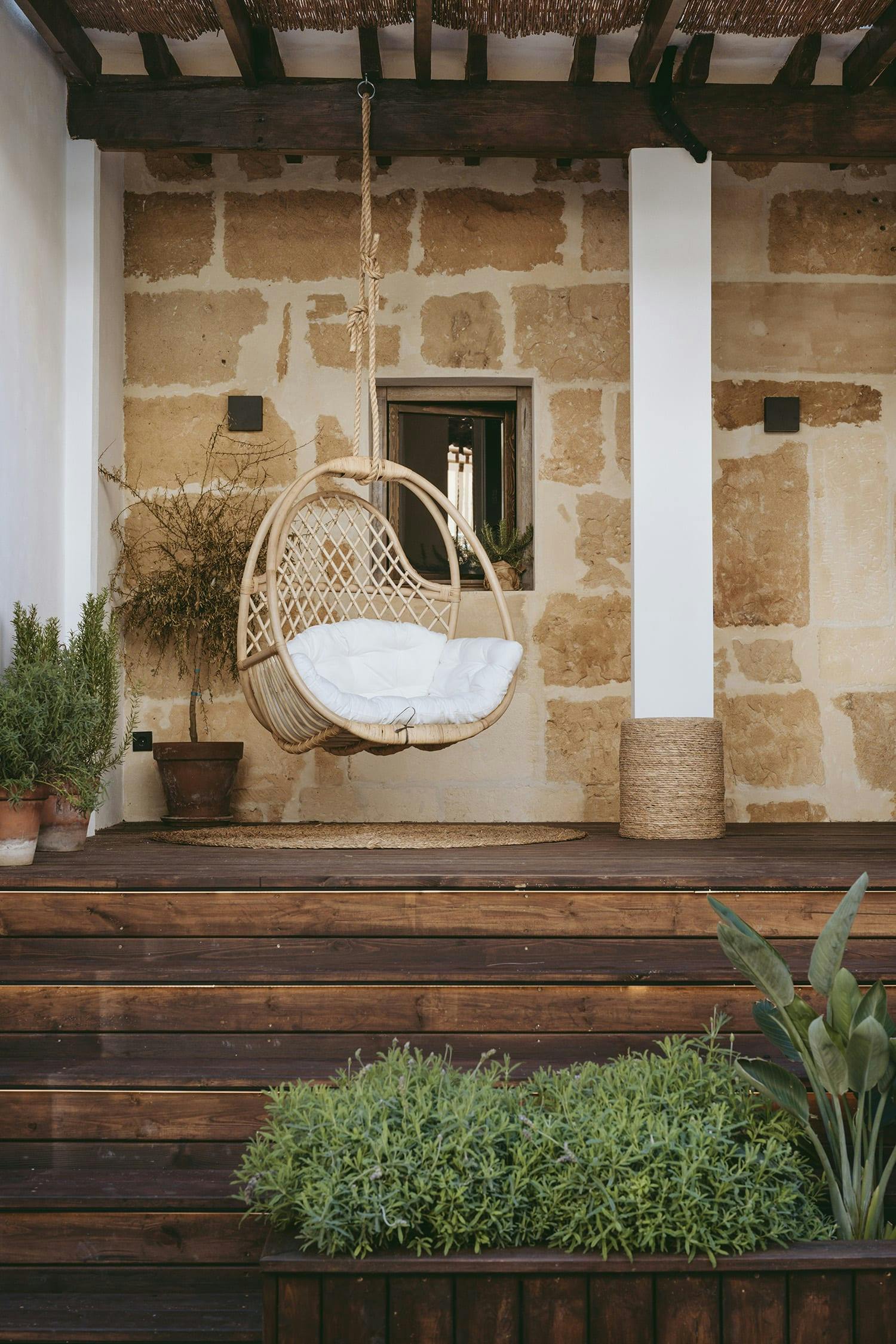A wooden deck with a wicker chair and a hanging basket of plants is shown in the image.