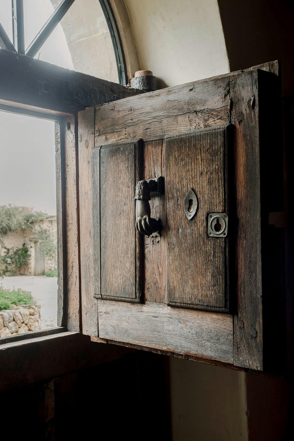 A wooden door with a metal lock is open, revealing a view of a field outside.