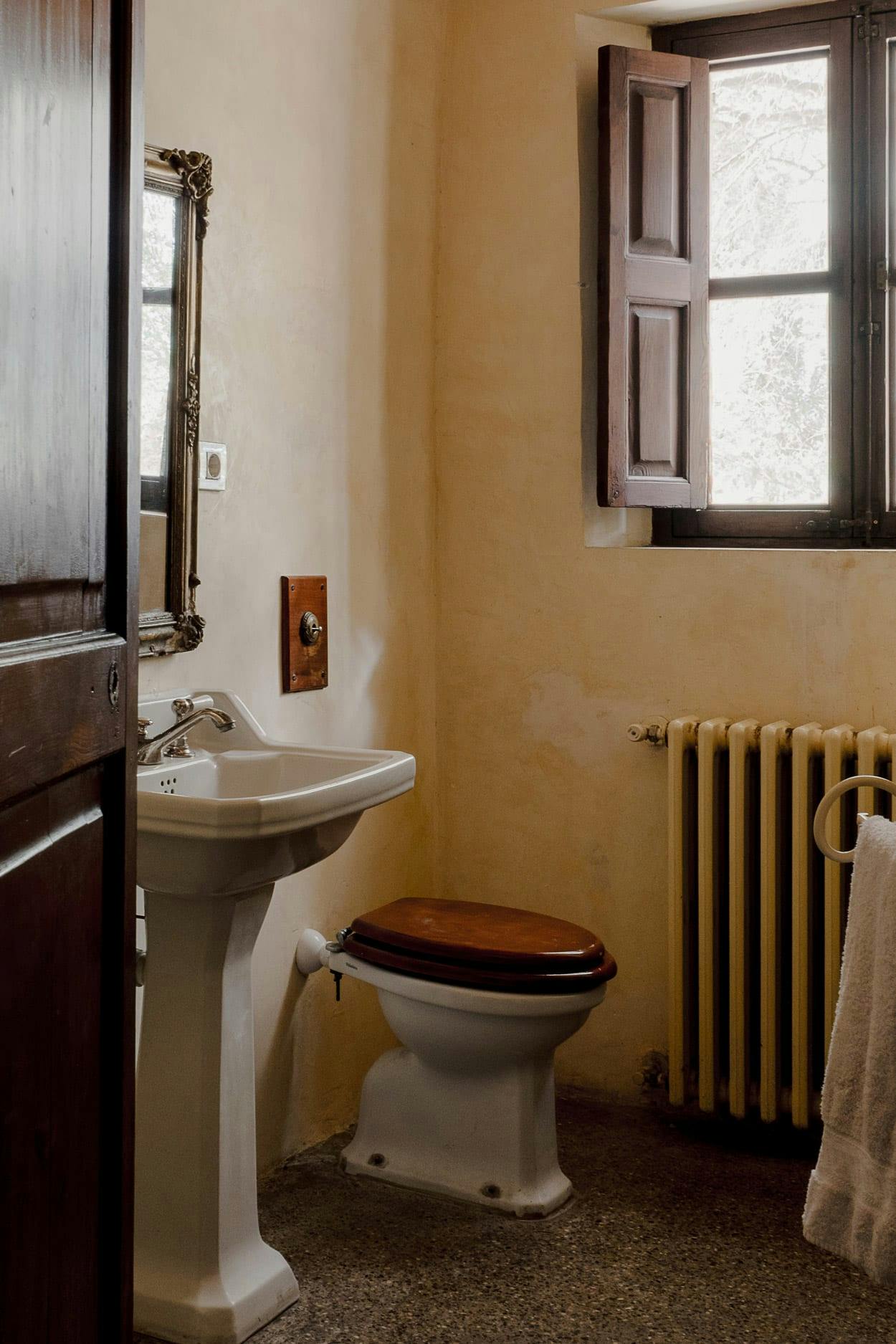 The image features a small, old-fashioned bathroom with a white toilet, sink, and radiator.