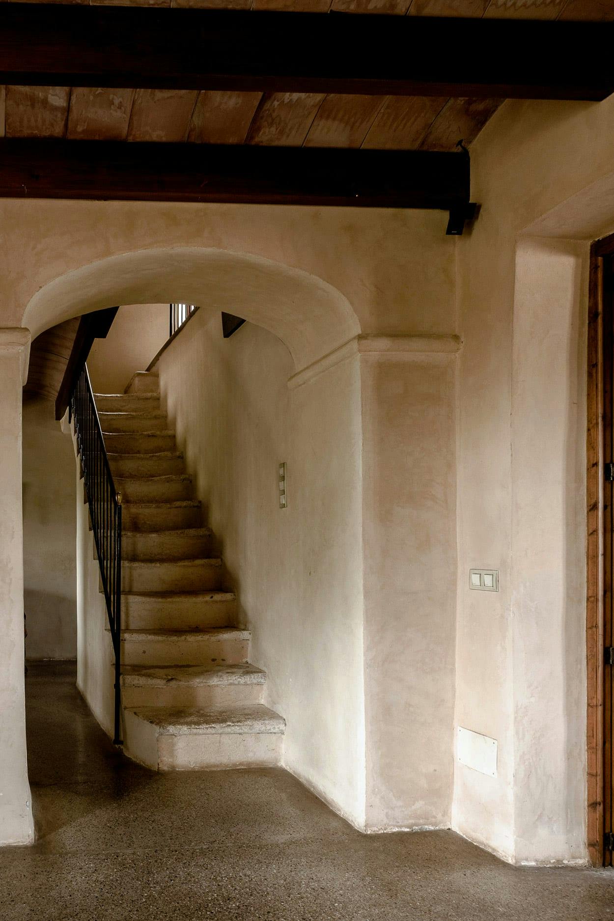 A long, narrow, and empty hallway with a staircase leading up to a doorway is depicted in the image.