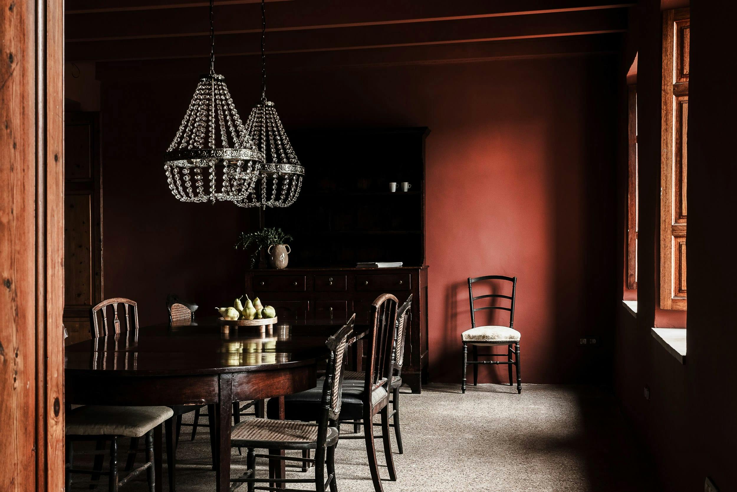 The image features a dark room with a long hallway, a dining table with chairs, and a chandelier hanging from the ceiling.