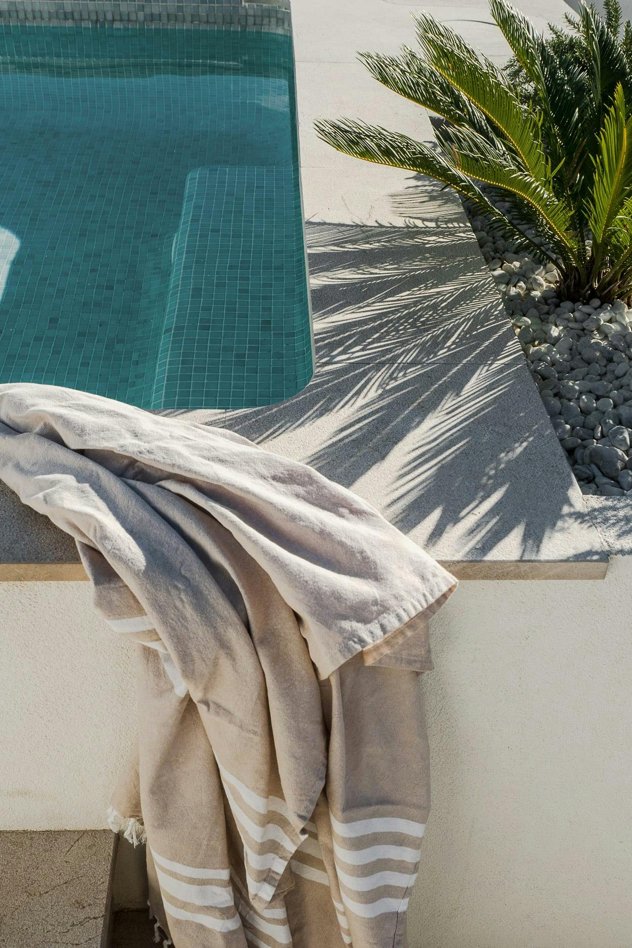A white towel is hanging on a railing outside, near a pool, and a palm tree, creating a relaxing and inviting atmosphere.