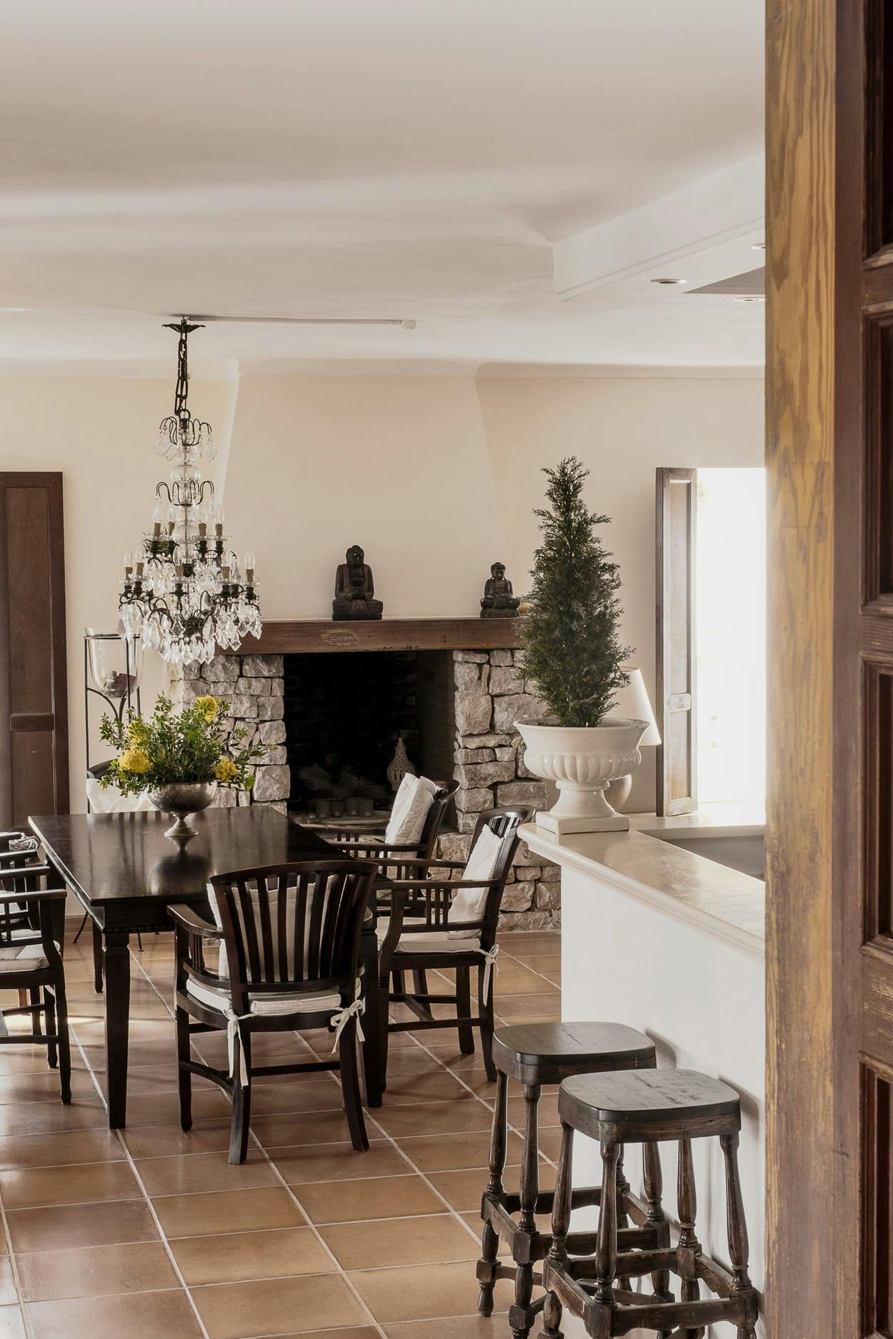 The image features a spacious living room with a fireplace, a dining table, and a chandelier.
