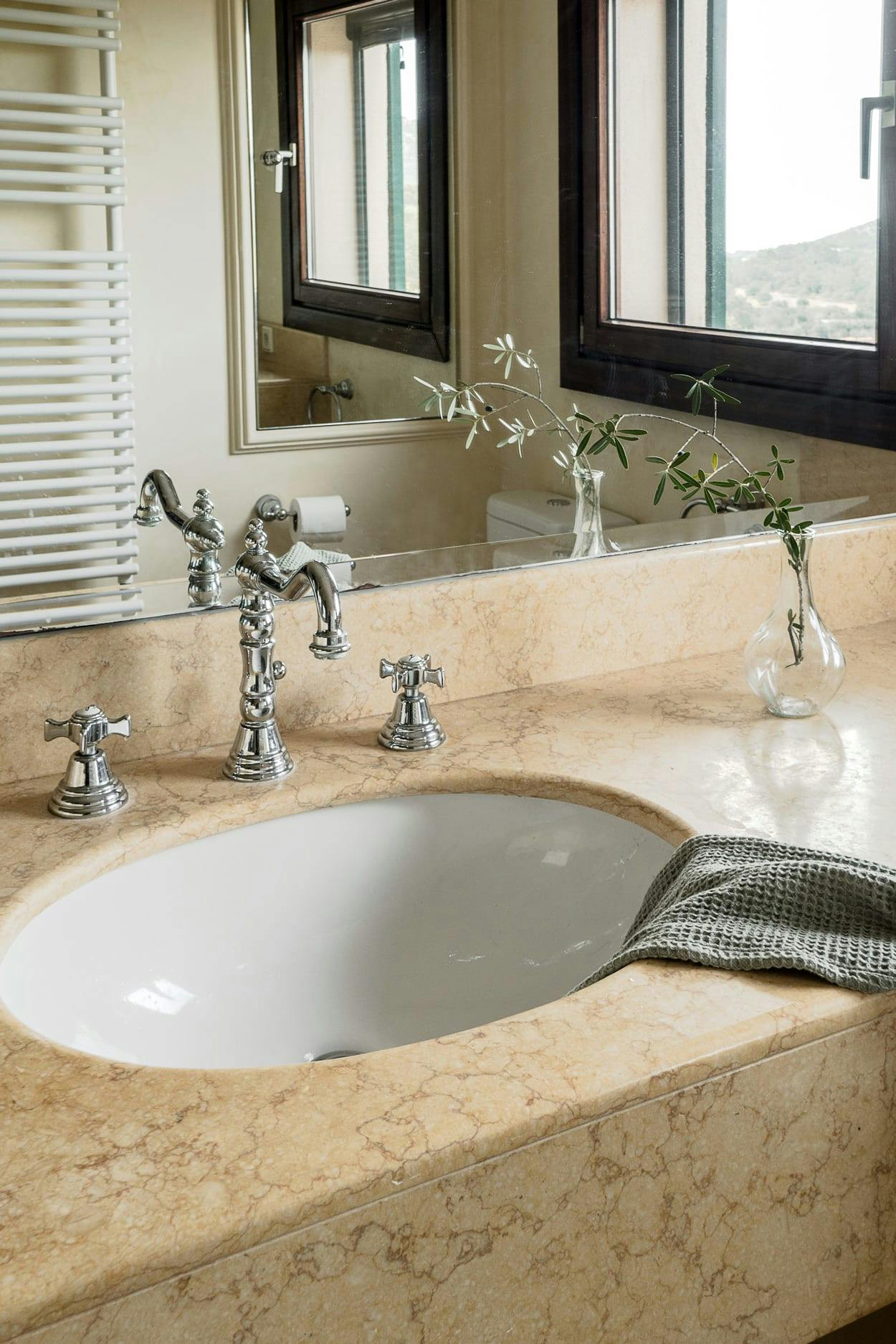 The image features a large, marble bathroom sink with a mirror above it, and a large window in the background.