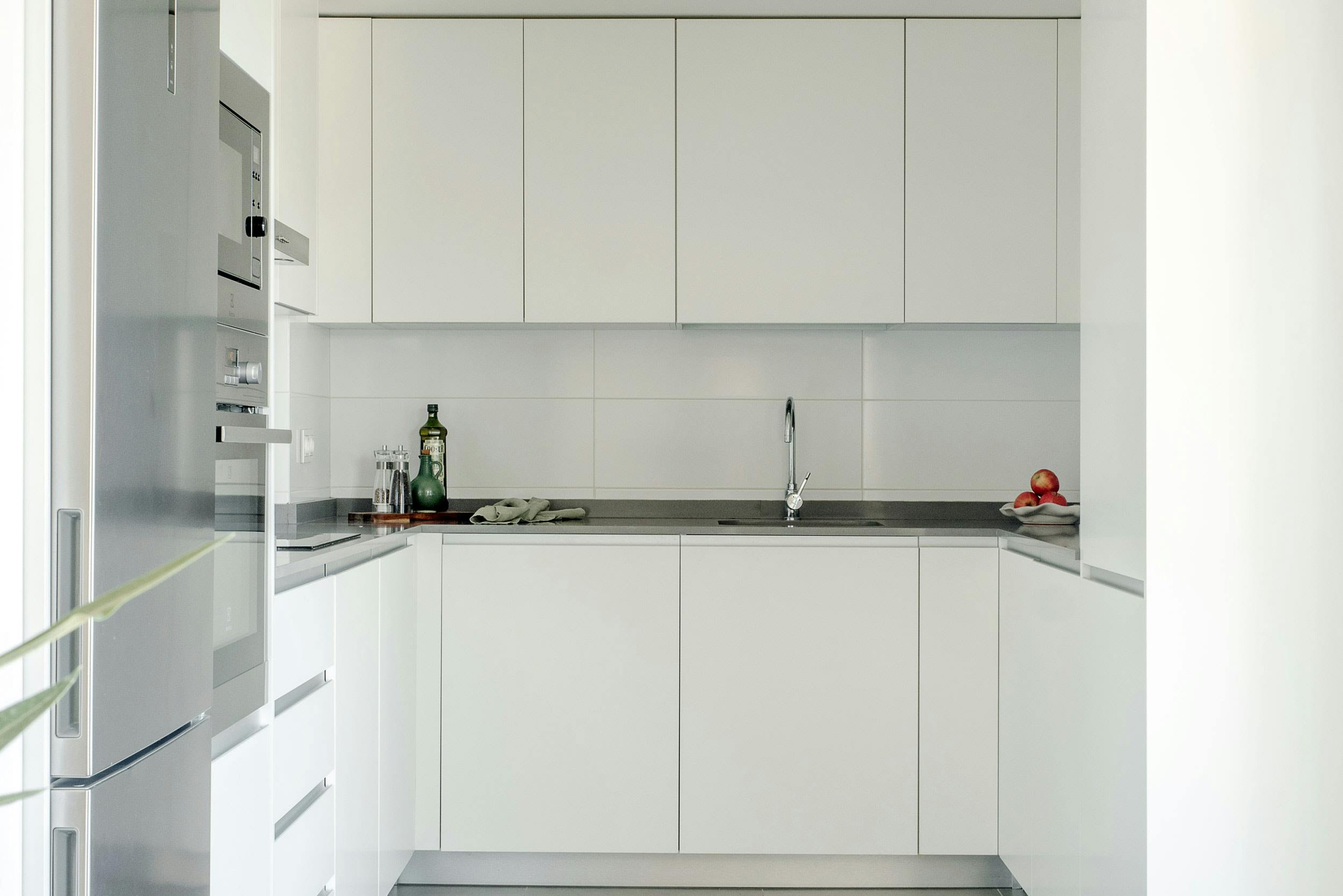 The image features a clean, white kitchen with a stainless steel sink, a white countertop, and a white cabinet.
