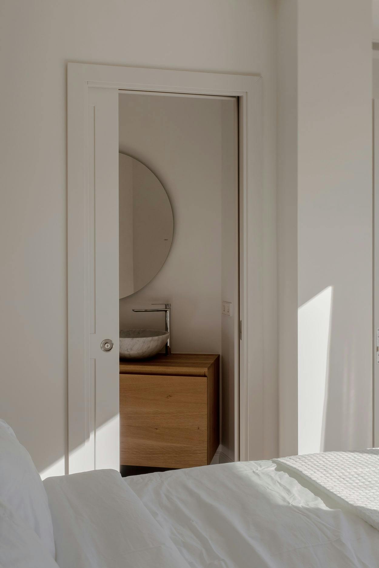 The image features a bedroom with a neatly made bed, a mirror, a dresser, and a door.