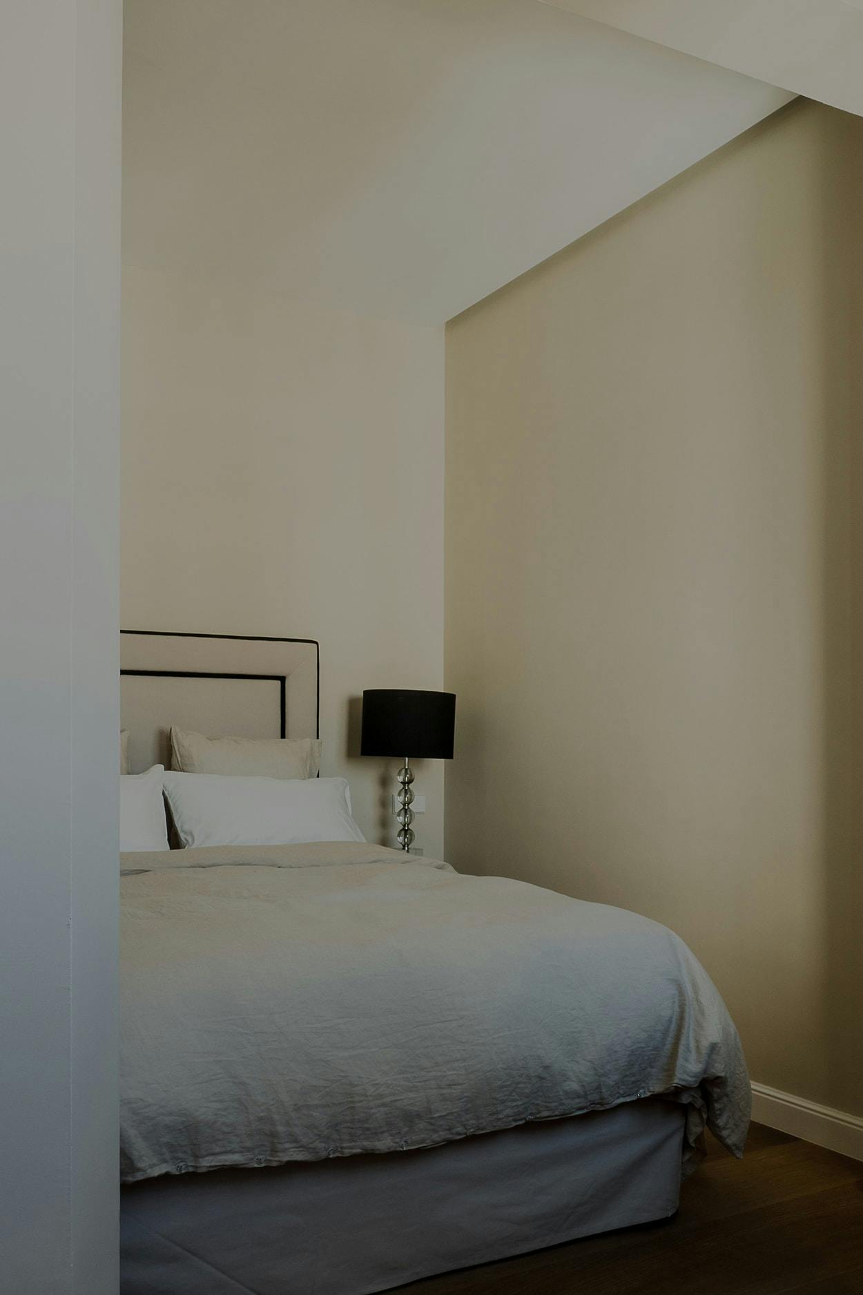 The image features a neatly made bed with a white comforter and pillows, placed next to a wall.