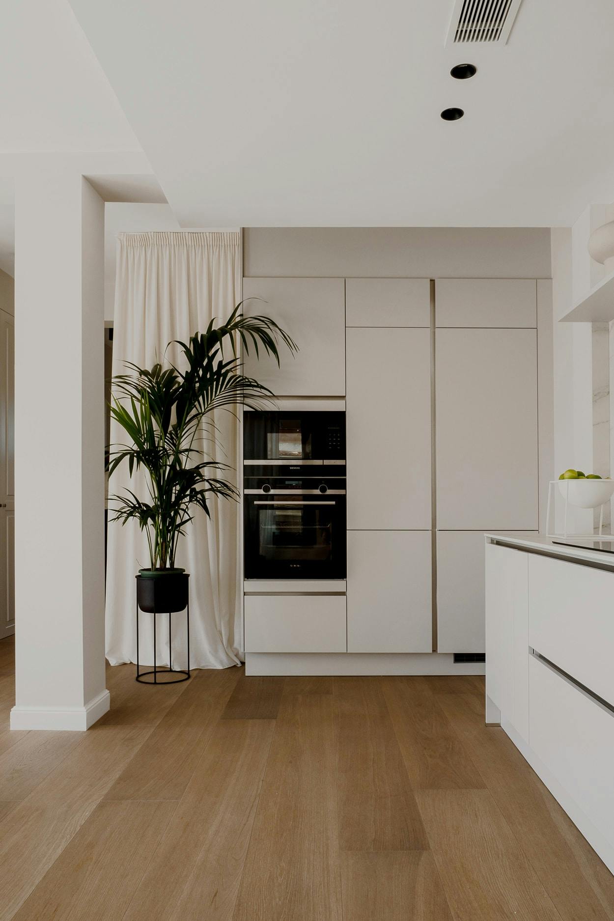 The image features a modern, white kitchen with a black countertop, a stainless steel oven, a microwave, a sink, and a potted plant.