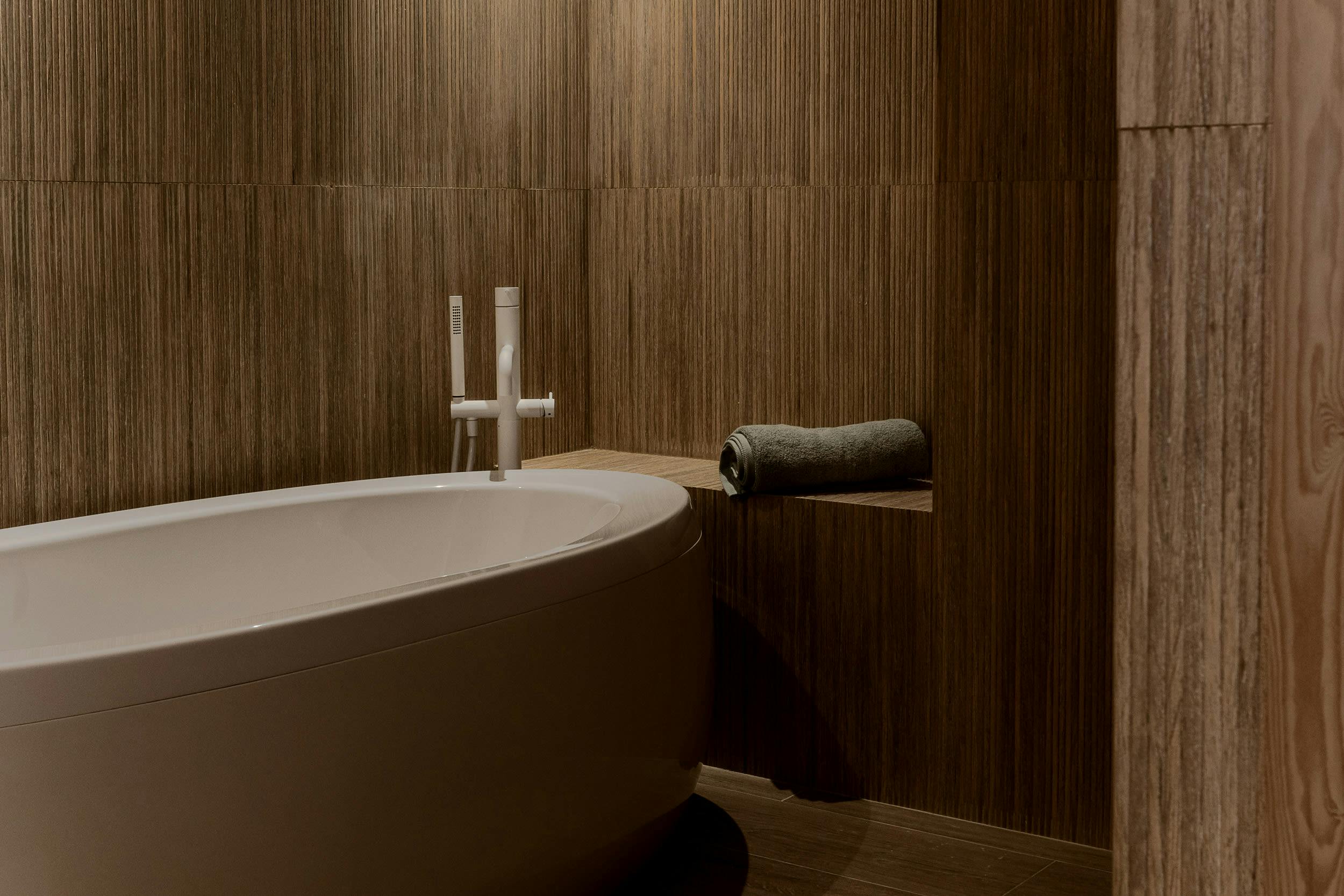 The image features a large, white bathtub in a bathroom with brown walls, a wooden wall, and a wooden floor.