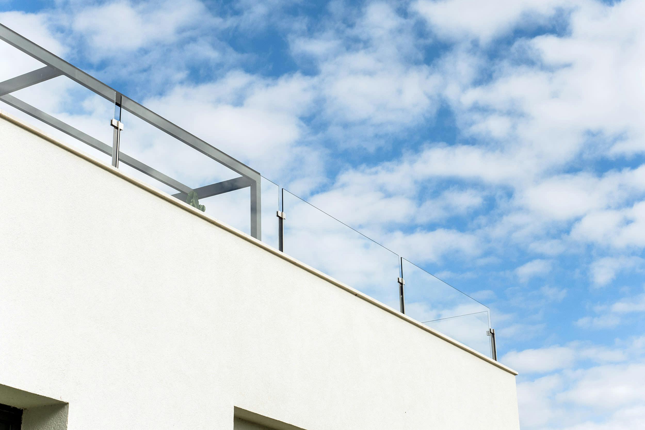 A white building with a metal railing on the side is set against a blue sky with clouds, creating a visually appealing and serene scene.