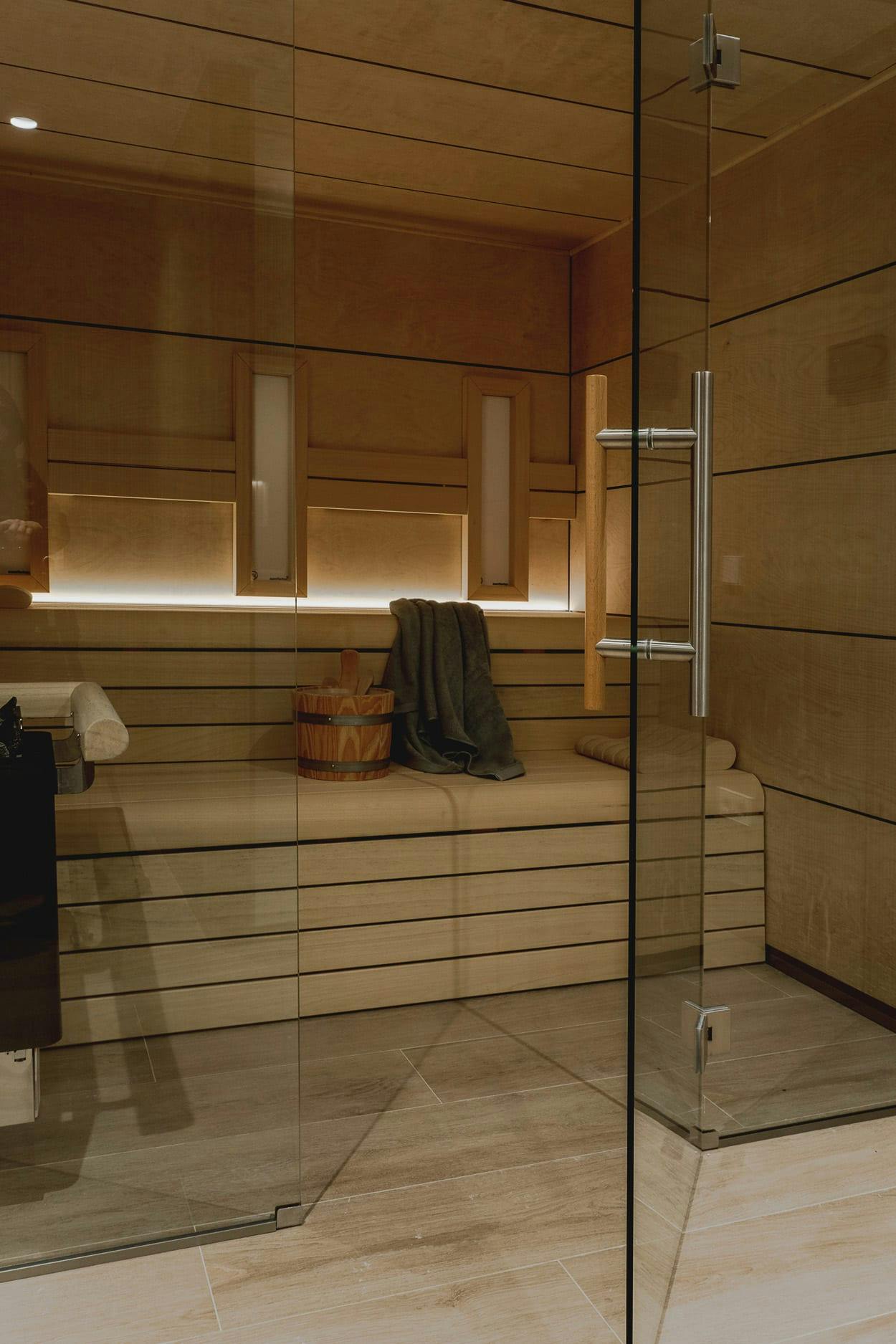 The image features a large, modern bathroom with a glass shower stall, a toilet, and a sink. The bathroom is well-lit and has a variety of towels and a handbag placed on the floor.