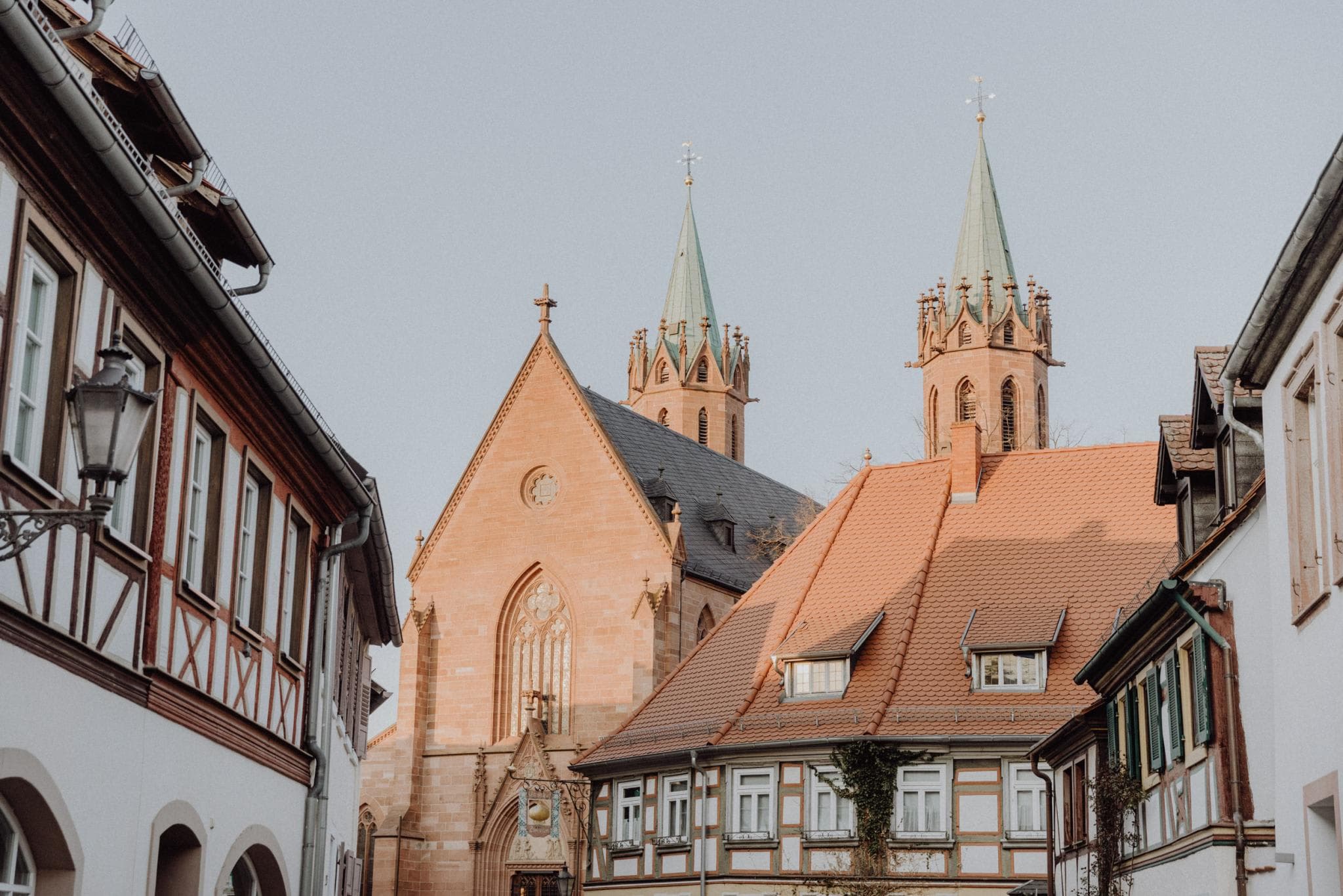The image features a picturesque town with a large, old church with a steeple and a clock tower. The town is surrounded by old buildings, and there are several people walking around.