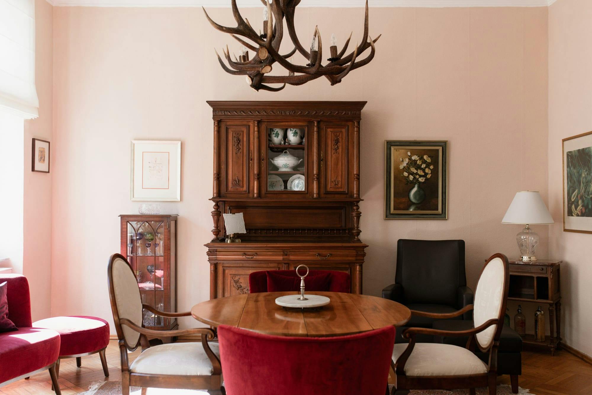 The image features a cozy living room with a wooden dining table, chairs, a TV, and a large antler chandelier.